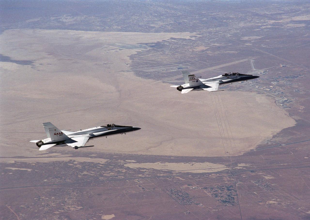 Flying an Autonomous Formation Flight mission, two F/A-18s from the NASA Dryden Flight Research Center, Edwards, California, gain altitude near Rogers Dry Lake.