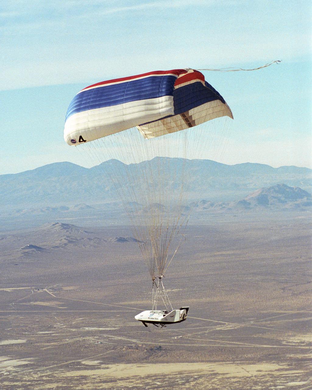 The X-38 prototype of the Crew Return Vehicle for the International Space Station is suspended under its giant 7,500-square-foot parafoil during its eighth free flight on Thursday, Dec. 13, 2001. A portion of the descent was flown by remote control by a NASA astronaut from a ground vehicle configured like the CRV's interior before the X-38 made an autonomous landing on Rogers Dry Lake.