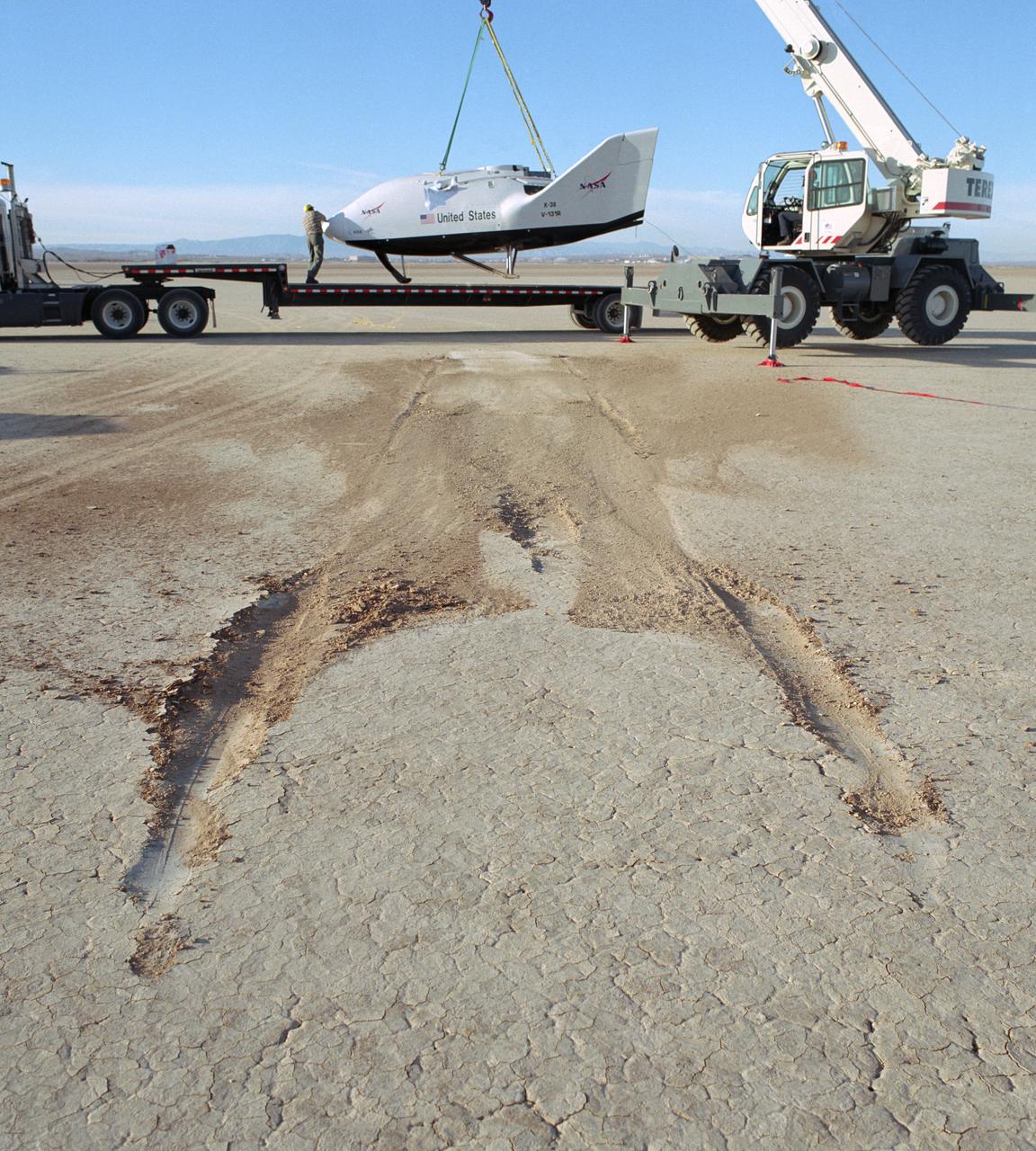The NASA X-38 is picked up from its dry lakebed landing site following its successful eighth free flight test mission December 13, 2001. Skid marks in the ground show the X-38's landing path.