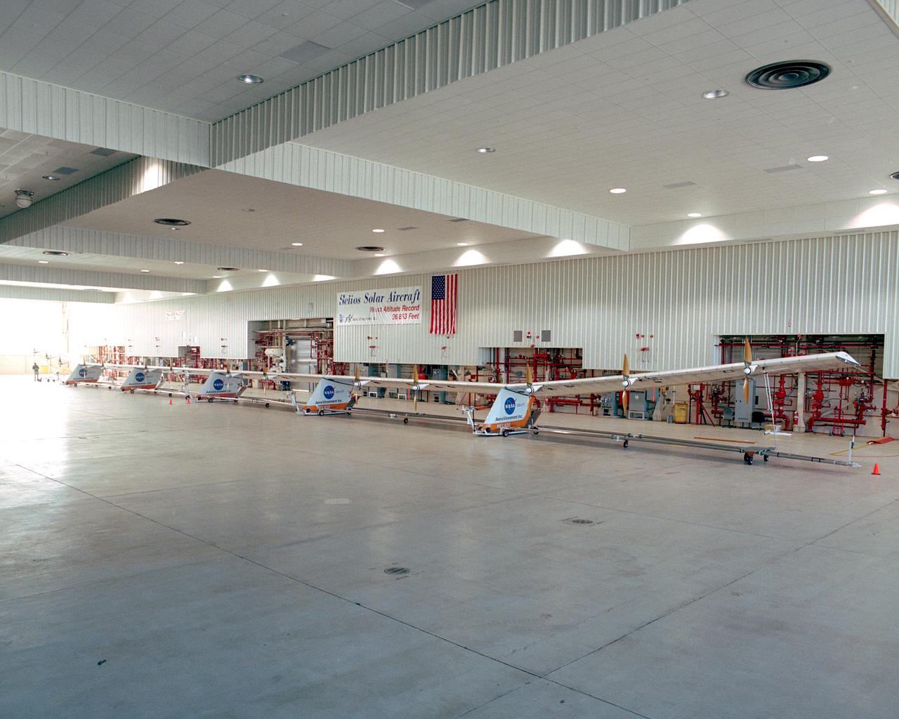 The Helios Prototype flying wing stretches almost the full length of the 300-foot-long hangar at NASA's Dryden Flight Research Center, Edwards, California. The 247-foot span solar-powered aircraft, resting on its ground maneuvering dolly, was on display for a visit of NASA Administrator Sean O'Keefe and other NASA officials on January 31, 2002. The unique solar-electric flying wing reached an altitude of 96,863 feet during an almost 17-hour flight near Hawaii on August 13, 2001, a world record for sustained horizontal flight by a non-rocket powered aircraft. Developed by AeroVironment, Inc., under NASA's Environmental Research Aircraft and Sensor Technology (ERAST) project, the Helios Prototype is the forerunner of a planned fleet of slow-flying, long duration, high-altitude uninhabited aerial vehicles (UAV) which can serve as "atmospheric satellites," performing Earth science missions or functioning as telecommunications relay platforms in the stratosphere.