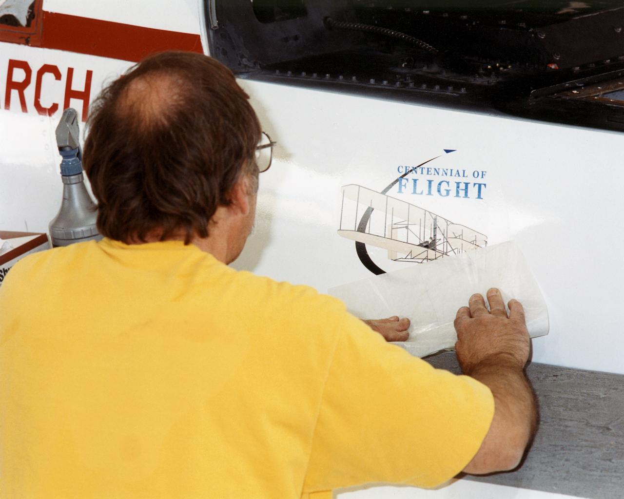 NASA aircraft technician Don Herman completes placement of the first official U.S. Centennial of Flight Commission logo on an aircraft, Dryden's Active Aeroelastic Wing (AAW) F/A-18.
