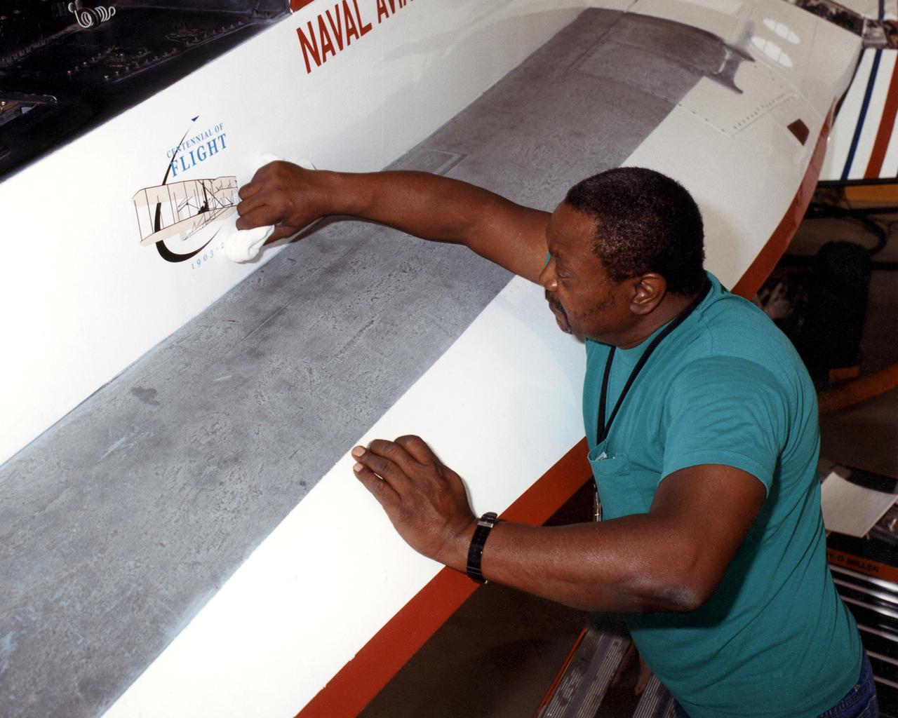 NASA aircraft technician Donte Warren completes placement of the first official U.S. Centennial of Flight Commission logo on an aircraft, Dryden's Active Aeroelastic Wing (AAW) F/A-18.