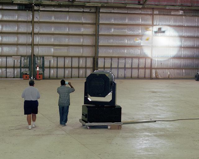 NASA image: Dryden Model Shop's Tony Frakowiak remotely flies an experimental model aircraft being powered by a spotlight operated by student intern Derrick Barrett.