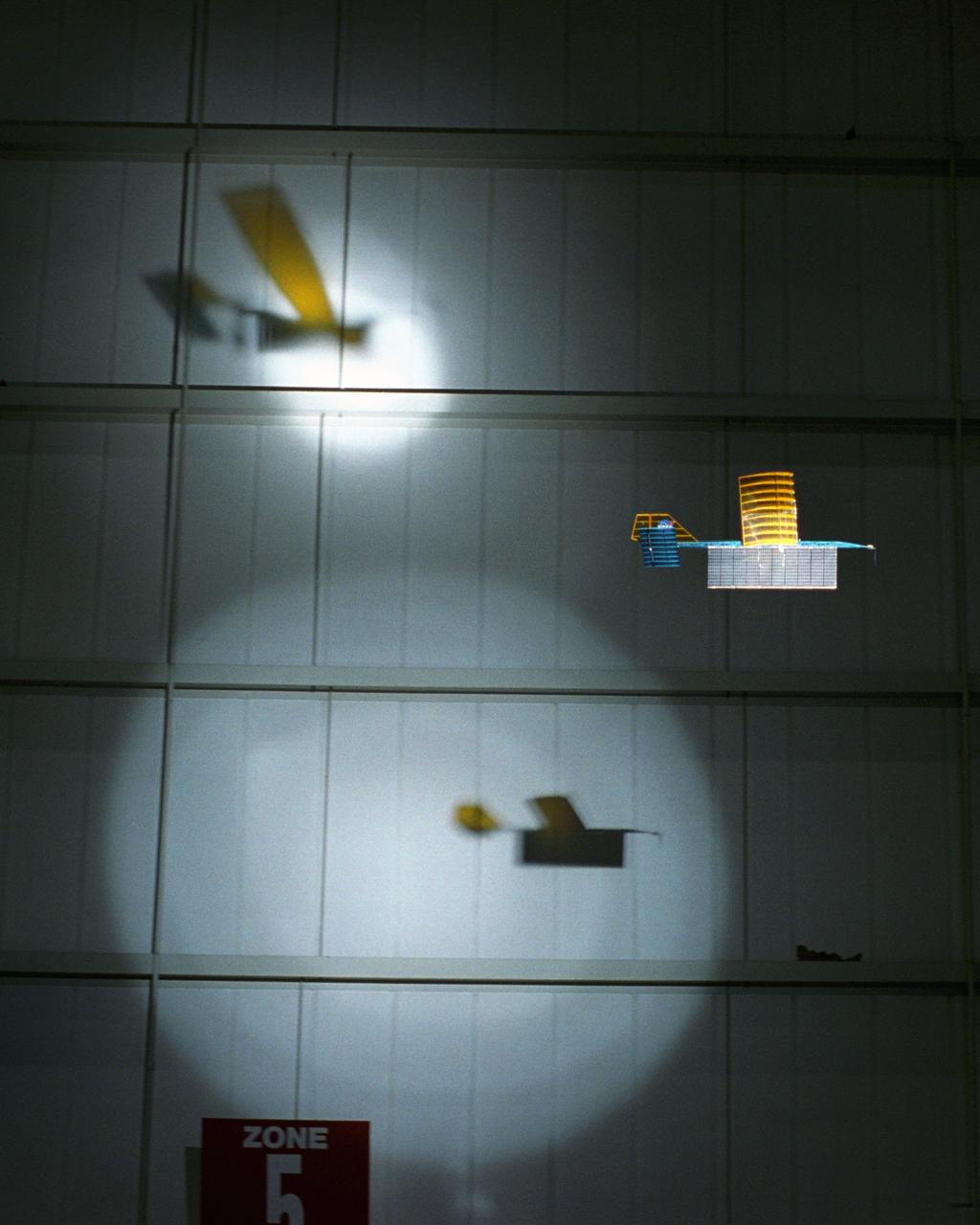 An experimental radio-controlled model aircraft casts two unique shadows as it flies inside a Dryden hangar using two spotlights as energy sources. This phase of testing was used to develop procedures and operations for "handing off" the aircraft between different sources of power.