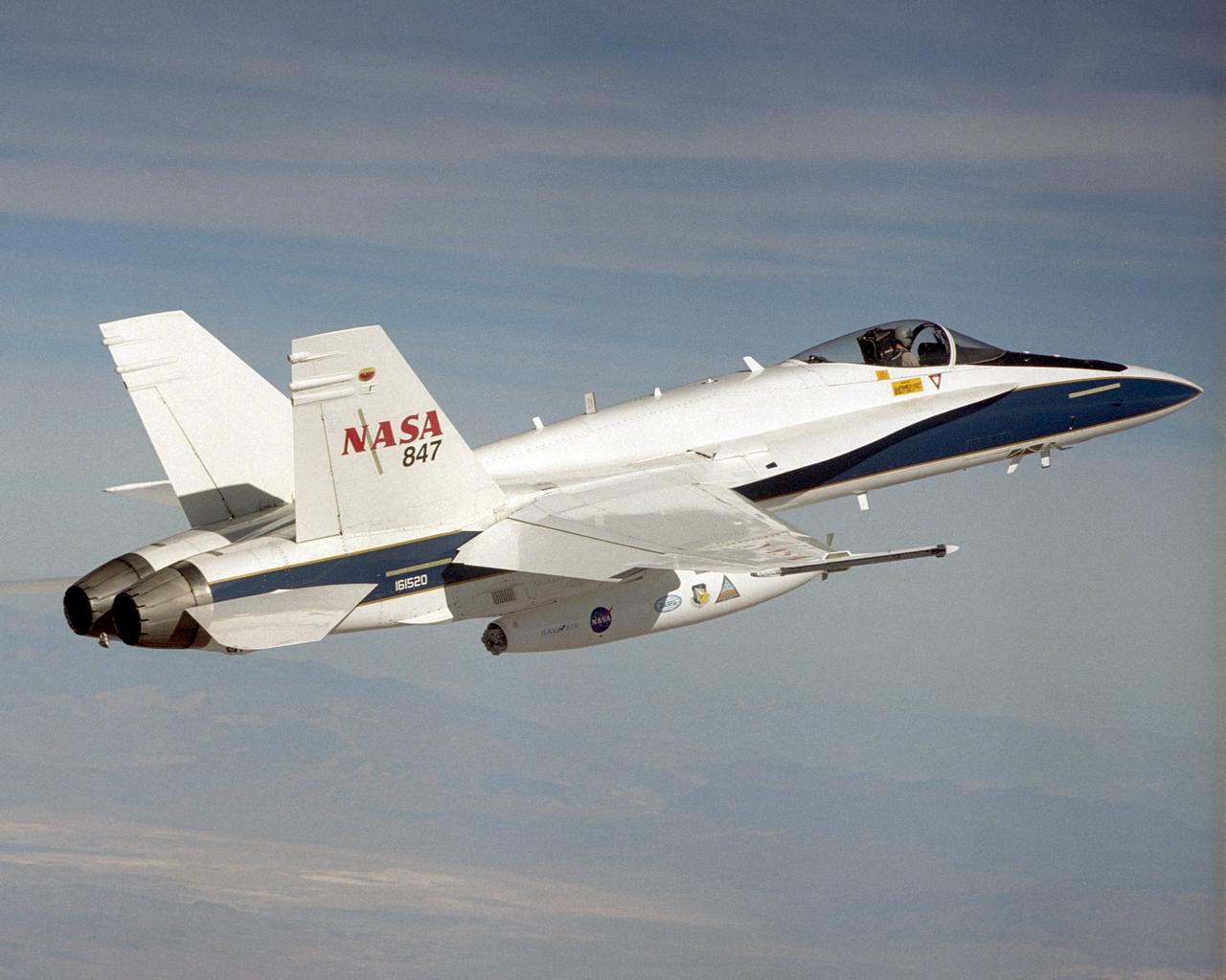 A NASA F/A-18 flies over the Dryden Flight Research Center and Rogers Dry Lake on December 11, 2002. The aircraft participated in the Automated Aerial Refueling (AAR) project. The 300-gallon aerial refueling store seen on the belly of the aircraft carries fuel and a refueling drogue. This aircraft acted as a tanker in the study to develop an aerodynamic model for future automated aerial refueling, especially of unmanned vehicles.