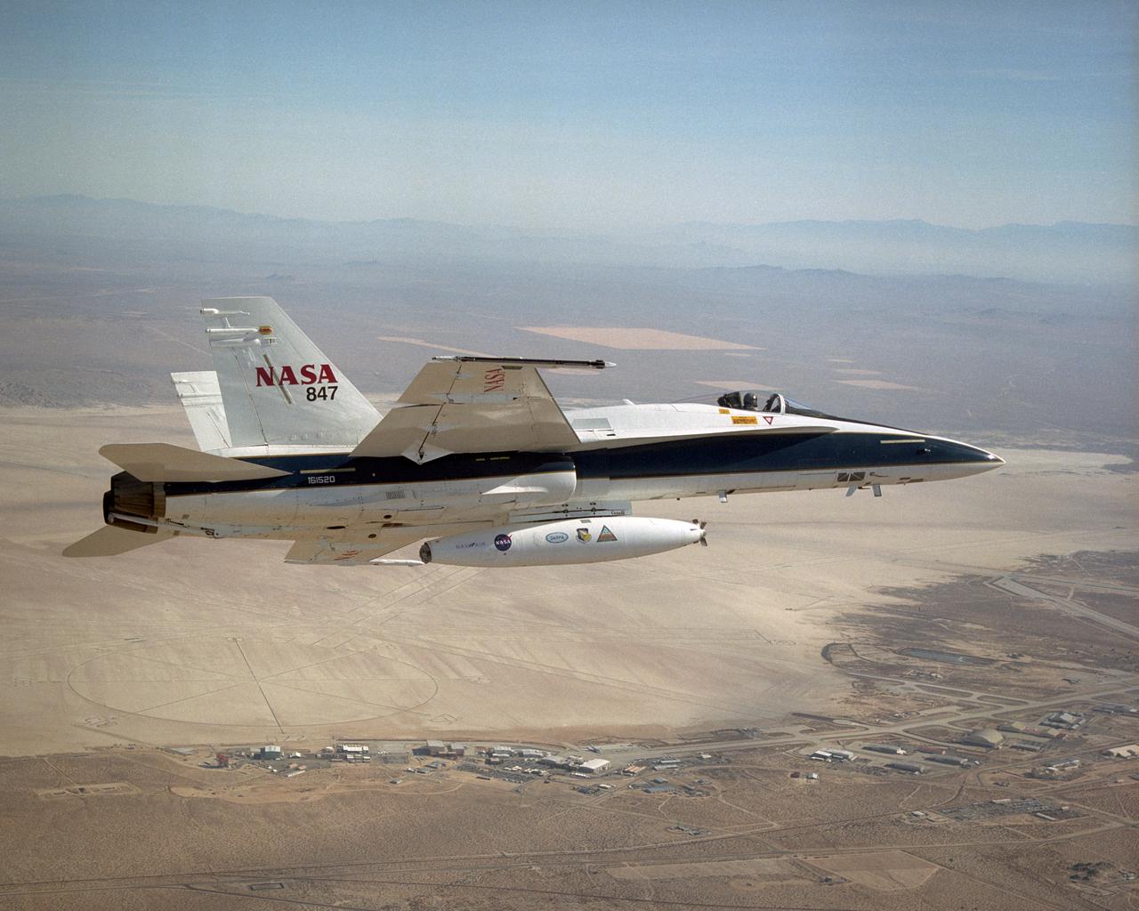 A NASA F/A-18 flies over the Dryden Flight Research Center and Rogers Dry Lake on December 11, 2002. The aircraft participated in the Automated Aerial Refueling (AAR) project. The 300-gallon aerial refueling store seen on the belly of the aircraft carries fuel and a refueling drogue. This aircraft acted as a tanker in the study to develop an aerodynamic model for future automated aerial refueling, especially of unmanned vehicles.