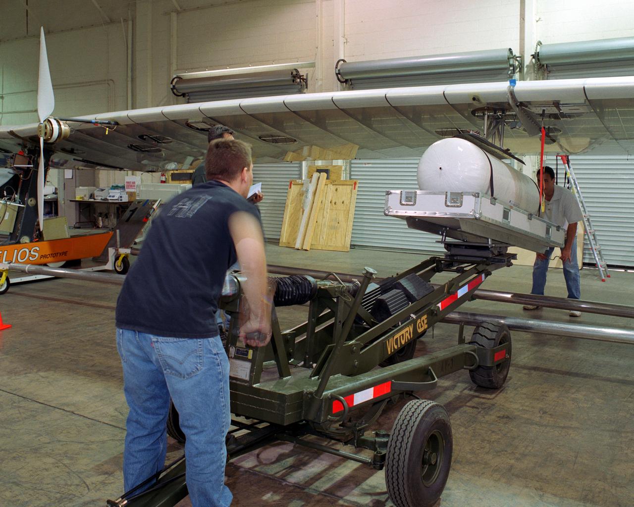 Technicians for AeroVironment, Inc., jack up a pressure tank to the wing of the Helios Prototype solar-electric flying wing. The tank carries pressurized hydrogen to fuel an experimental fuel cell system that powered the aircraft at night during an almost two-day long-endurance flight demonstration in the summer of 2003.