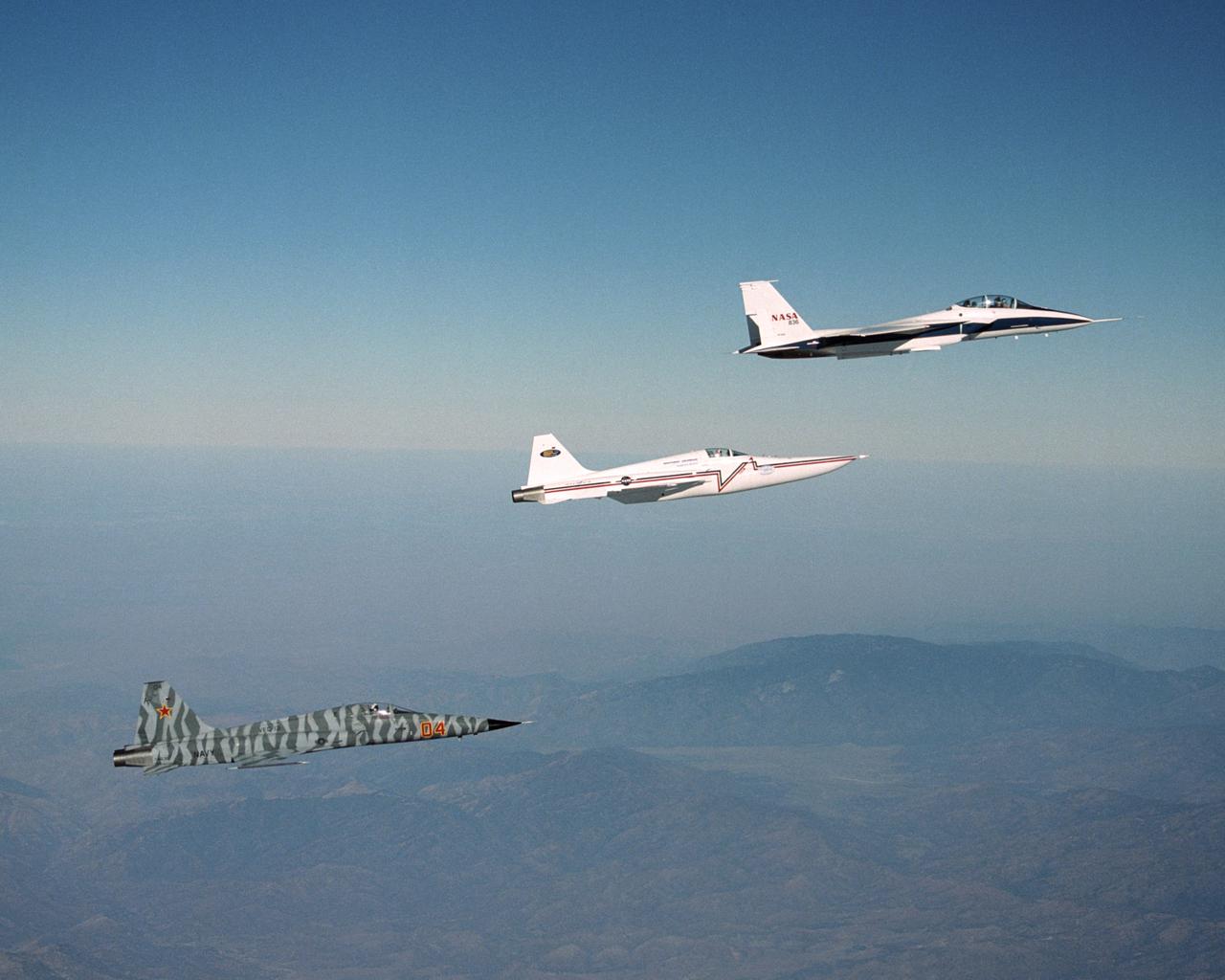 In a role-reversal, Northrop Grumman Corp.'s modified F-5E Shaped Sonic Boom Demonstration (SSBD) aircraft flies off the wing of NASA's F-15B Research testbed aircraft. The F-15B, from NASA's Dryden Flight Research Center, flew in the supersonic shockwave of the F-5E as part of the SSBD project. Following the two aircraft is an unmodified U.S. Navy F-5E used for baseline sonic boom measurements.