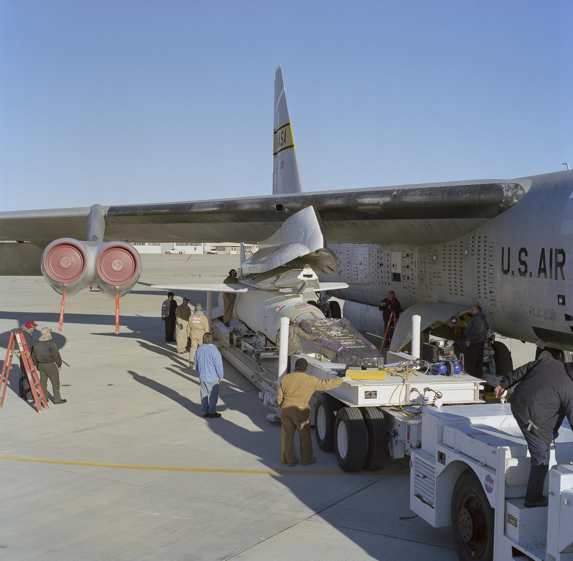 A rocket booster carrying an experimental aircraft on its nose are positioned under an aircraft wing.