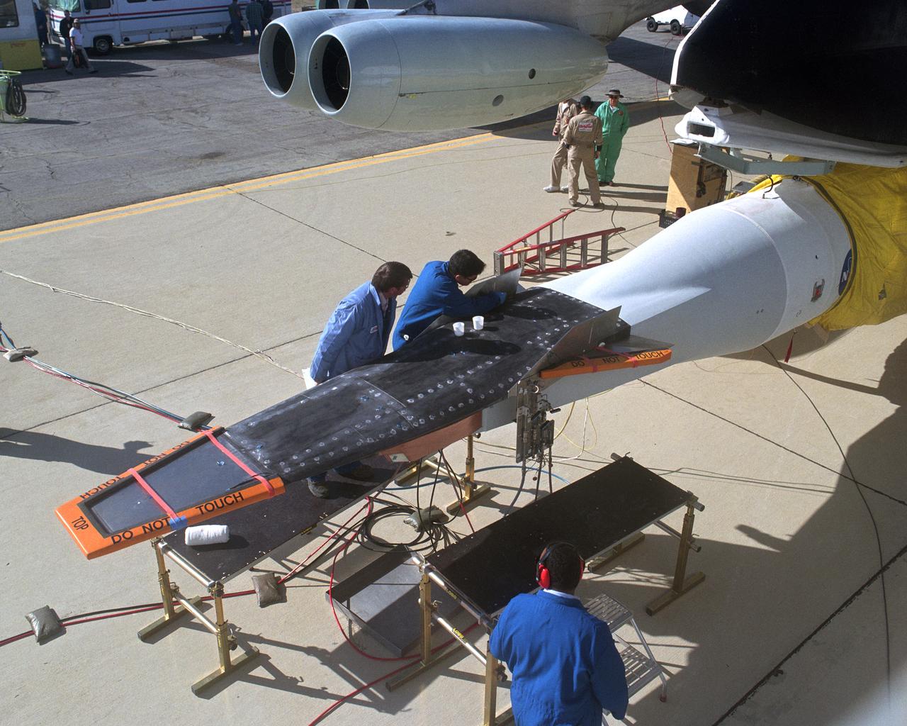 The second X-43A hypersonic research vehicle, mounted under the right wing of the B-52B launch aircraft, viewed from the B-52 cockpit. The crew is working on closing out the research vehicle, preparing it for flight.