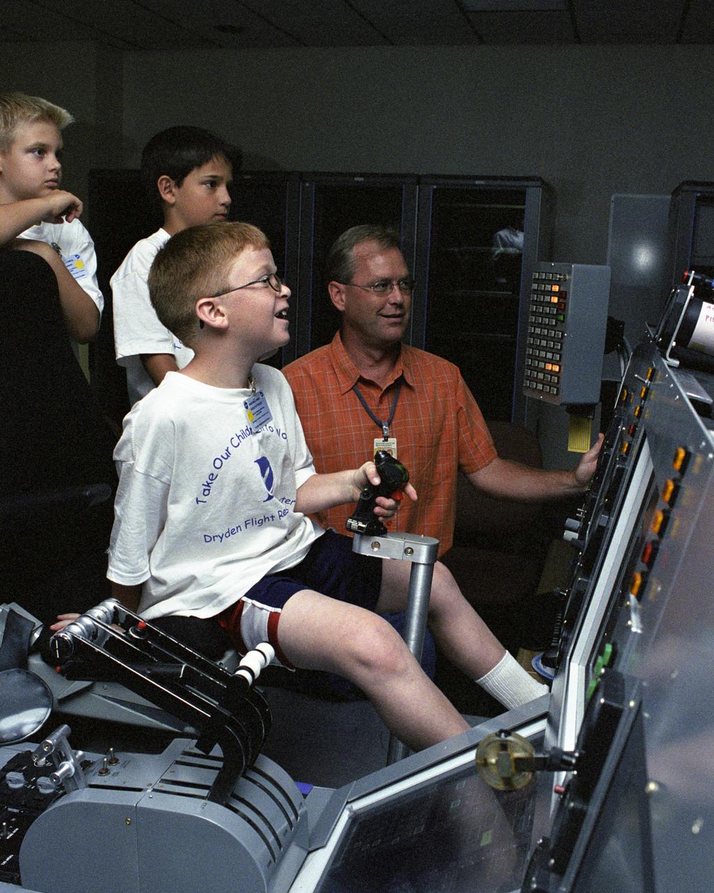 Eddie Patterson, a fourth-grade student at Tehachapi's Tompkins Elementary School, enjoyed "flying" a C-17 multi-engine aircraft simulator during Take Your Children to Work Day June 22 at NASA Dryden Flight Research Center while NASA Dryden engineer Ken Norlin and other students look on.