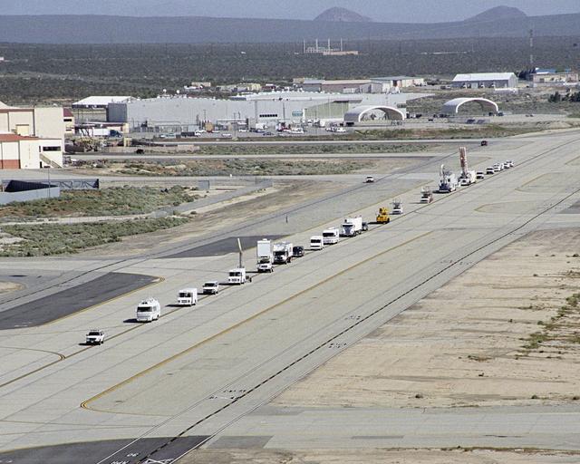 NASA image: A long string of specialized NASA vehicles convoys down a taxiway at Edwards Air Force Base to begin a Space Shuttle rescue and recovery training exercise