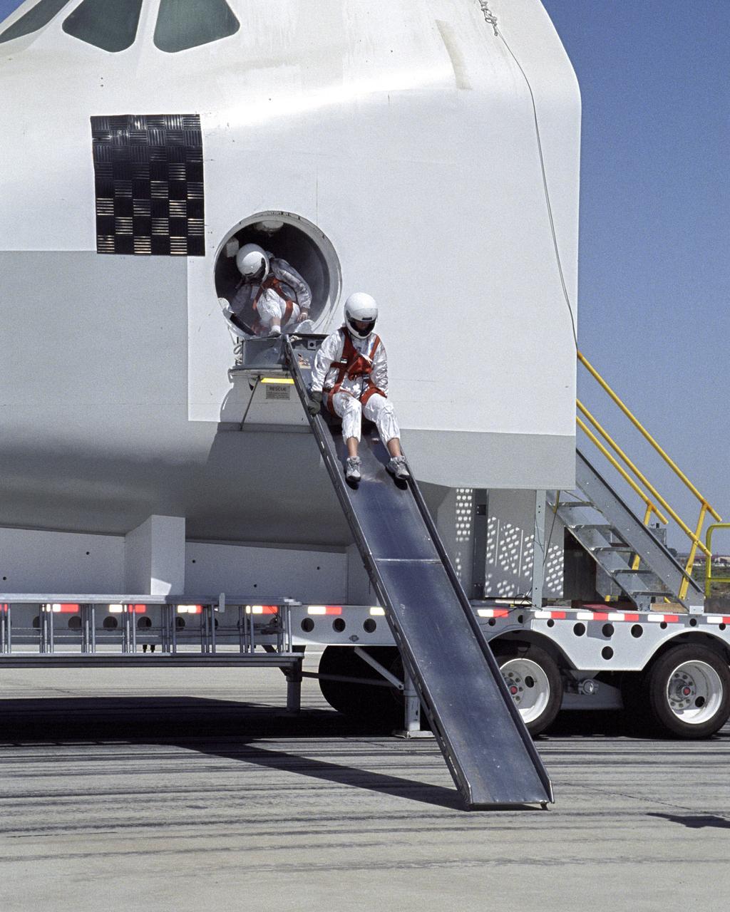 A volunteer "astronaut" starts down an exit slide from a Space Shuttle crew compartment mockup during a rescue and recovery training exercise.