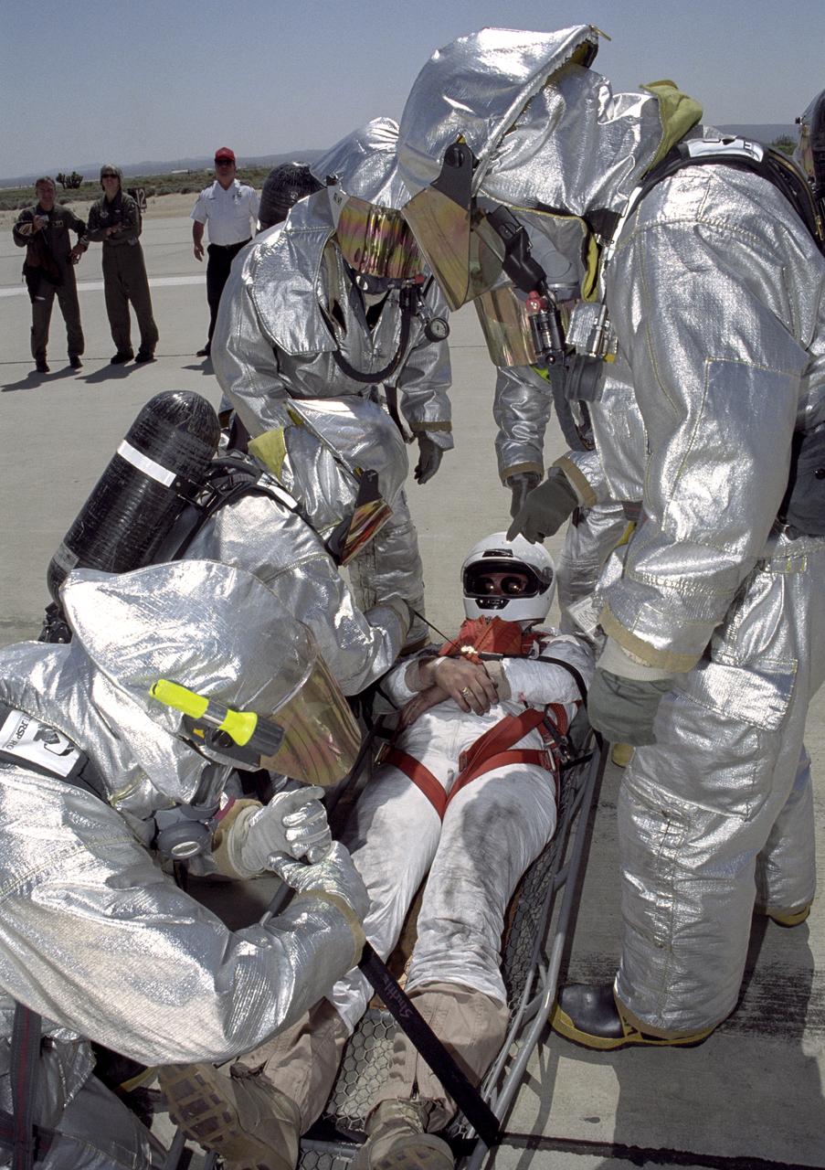 Clad in full thermal protection suits, Air Force fire-rescue crews strap a stand-in "astronaut" into a litter during a Space Shuttle rescue training exercise at Edwards AFB.