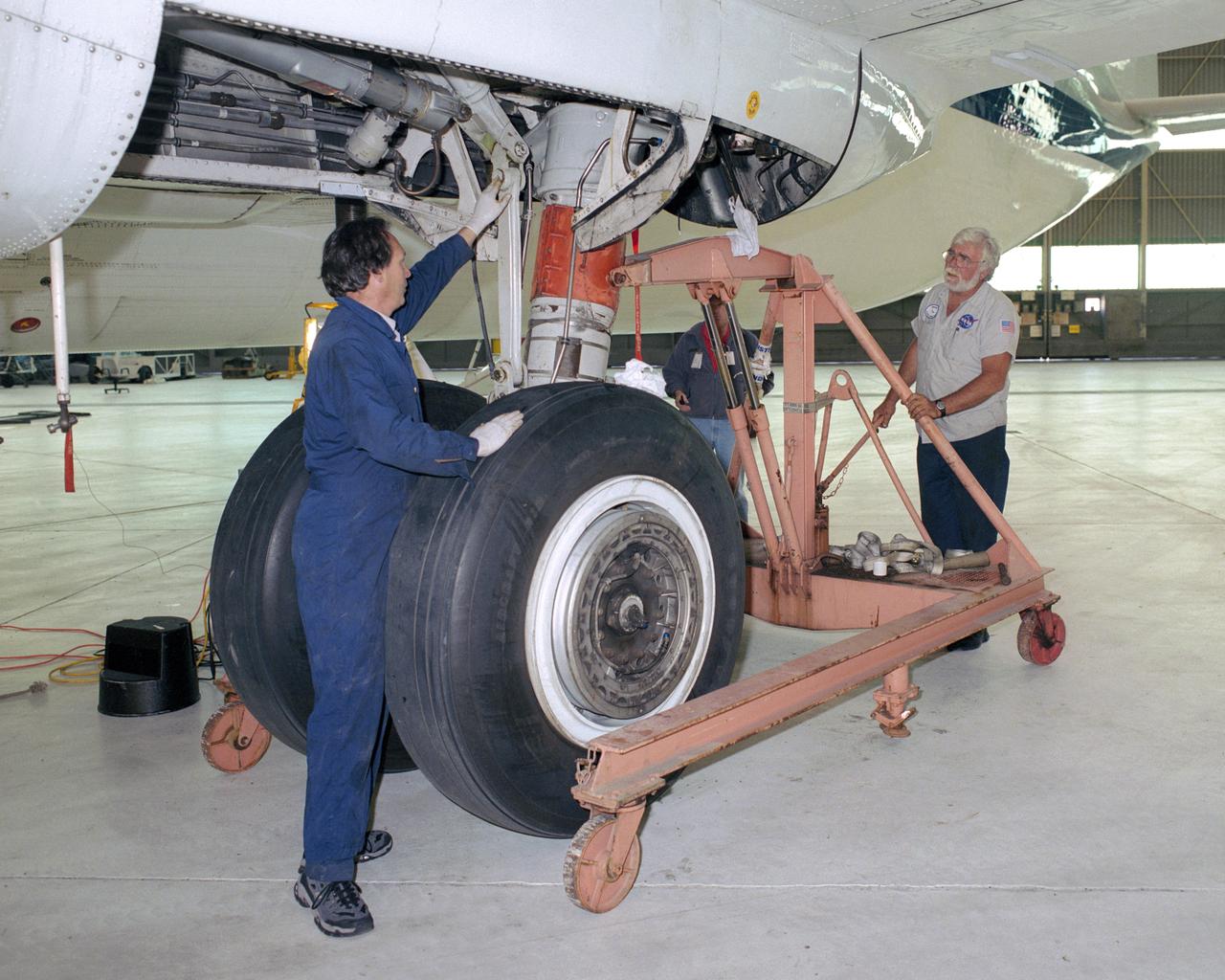 JSC technicians David Wyckoff and Tom Gordon carefully maneuver their equipment into place as they prepare to remove the Super Guppy's left main landing gear.