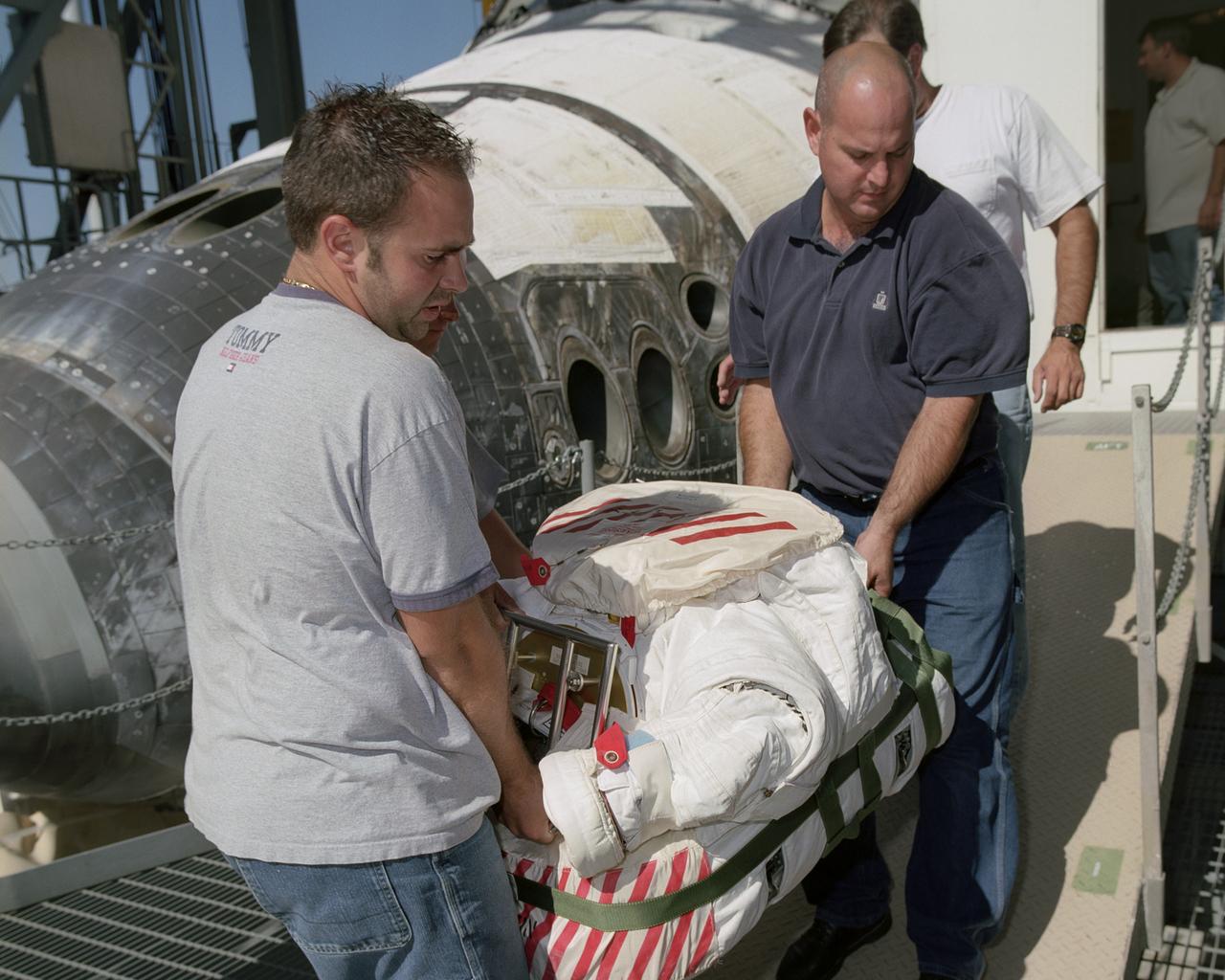 Flight Crew Systems Technicians Ray Smith and Raphael Rodriguez remove one of the Extravehicular Mobility Units, or EMUs, from the Space Shuttle Discovery after it's successful landing at NASA's Dryden Flight Research Center. The Space Shuttles receive post-flight servicing in the Mate-Demate Device (MDD) following landings at NASA's Dryden Flight Research Center, Edwards, California. The gantry-like MDD structure is used for servicing the shuttle orbiters in preparation for their ferry flight back to the Kennedy Space Center in Florida, including mounting the shuttle atop NASA's modified Boeing 747 Shuttle Carrier Aircraft.  Space Shuttle Discovery landed safely at NASA's Dryden Flight Research Center at Edwards Air Force Base in California at 5:11:22 a.m. PDT, August 9, 2005, following the very successful 14-day STS-114 return to flight mission.  During their two weeks in space, Commander Eileen Collins and her six crewmates tested out new safety procedures and delivered supplies and equipment the International Space Station.  Discovery spent two weeks in space, where the crew demonstrated new methods to inspect and repair the Shuttle in orbit. The crew also delivered supplies, outfitted and performed maintenance on the International Space Station. A number of these tasks were conducted during three spacewalks.  In an unprecedented event, spacewalkers were called upon to remove protruding gap fillers from the heat shield on Discovery's underbelly. In other spacewalk activities, astronauts installed an external platform onto the Station's Quest Airlock and replaced one of the orbital outpost's Control Moment Gyroscopes.  Inside the Station, the STS-114 crew conducted joint operations with the Expedition 11 crew. They unloaded fresh supplies from the Shuttle and the Raffaello Multi-Purpose Logistics Module. Before Discovery undocked, the crews filled Raffeallo with unneeded items and returned to Shuttle payload bay.  Discovery launched on July 26 and spent almost 14