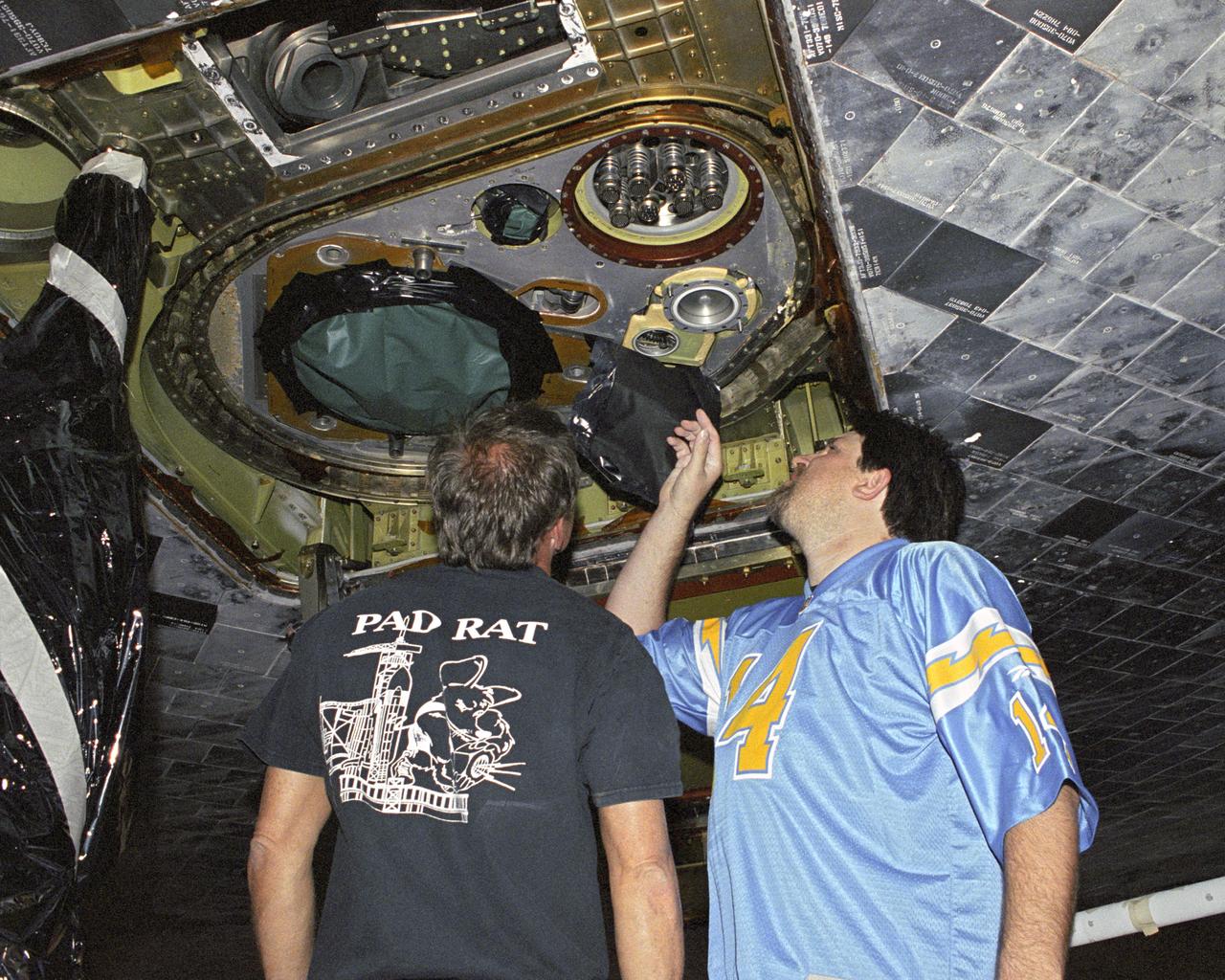 Robert 'Skip' Garrett; main propulsion advanced systems technician, and Chris Jacobs; main propulsion systems engineering technician, inspect external tank attachment fittings on the Space Shuttle Discovery as part of it's post-flight processing at NASA's Dryden Flight Research Center. The Space Shuttles receive post-flight servicing in the Mate-Demate Device (MDD) following landings at NASA's Dryden Flight Research Center, Edwards, California. The gantry-like MDD structure is used for servicing the shuttle orbiters in preparation for their ferry flight back to the Kennedy Space Center in Florida, including mounting the shuttle atop NASA's modified Boeing 747 Shuttle Carrier Aircraft.  Space Shuttle Discovery landed safely at NASA's Dryden Flight Research Center at Edwards Air Force Base in California at 5:11:22 a.m. PDT, August 9, 2005, following the very successful 14-day STS-114 return to flight mission.  During their two weeks in space, Commander Eileen Collins and her six crewmates tested out new safety procedures and delivered supplies and equipment the International Space Station.  Discovery spent two weeks in space, where the crew demonstrated new methods to inspect and repair the Shuttle in orbit. The crew also delivered supplies, outfitted and performed maintenance on the International Space Station. A number of these tasks were conducted during three spacewalks.  In an unprecedented event, spacewalkers were called upon to remove protruding gap fillers from the heat shield on Discovery's underbelly. In other spacewalk activities, astronauts installed an external platform onto the Station's Quest Airlock and replaced one of the orbital outpost's Control Moment Gyroscopes.  Inside the Station, the STS-114 crew conducted joint operations with the Expedition 11 crew. They unloaded fresh supplies from the Shuttle and the Raffaello Multi-Purpose Logistics Module. Before Discovery undocked, the crews filled Raffeallo with unneeded items and returned to Shuttle pa