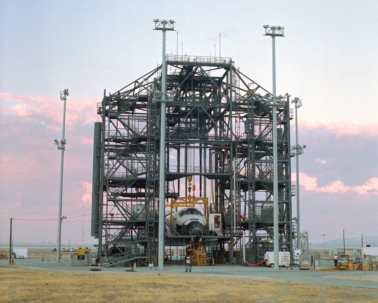 The sun sets on the Space Shuttle Discovery during post-flight processing in the Mate-Demate Device (MDD), following its landing at NASA's Dryden Flight Research Center in California. The gantry-like MDD structure is used for servicing the shuttle orbiters in preparation for their ferry flight back to the Kennedy Space Center in Florida, including mounting the shuttle atop NASA's modified Boeing 747 Shuttle Carrier Aircraft.  Space Shuttle Discovery landed safely at NASA's Dryden Flight Research Center at Edwards Air Force Base in California at 5:11:22 a.m. PDT, August 9, 2005, following the very successful 14-day STS-114 return to flight mission.  During their two weeks in space, Commander Eileen Collins and her six crewmates tested out new safety procedures and delivered supplies and equipment the International Space Station.  Discovery spent two weeks in space, where the crew demonstrated new methods to inspect and repair the Shuttle in orbit. The crew also delivered supplies, outfitted and performed maintenance on the International Space Station. A number of these tasks were conducted during three spacewalks.  In an unprecedented event, spacewalkers were called upon to remove protruding gap fillers from the heat shield on Discovery's underbelly. In other spacewalk activities, astronauts installed an external platform onto the Station's Quest Airlock and replaced one of the orbital outpost's Control Moment Gyroscopes.  Inside the Station, the STS-114 crew conducted joint operations with the Expedition 11 crew. They unloaded fresh supplies from the Shuttle and the Raffaello Multi-Purpose Logistics Module. Before Discovery undocked, the crews filled Raffeallo with unneeded items and returned to Shuttle payload bay.  Discovery launched on July 26 and spent almost 14 days on orbit.