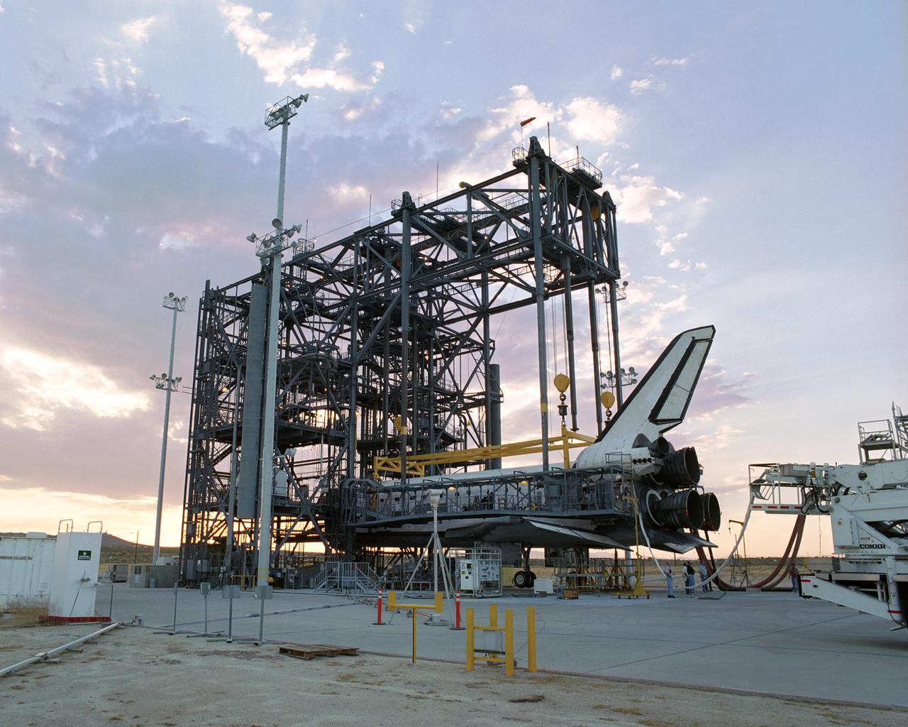 The sun sets on the Space Shuttle Discovery during post-flight processing in the Mate-Demate Device (MDD), following its landing at NASA's Dryden Flight Research Center in California. The gantry-like MDD structure is used for servicing the shuttle orbiters in preparation for their ferry flight back to the Kennedy Space Center in Florida, including mounting the shuttle atop NASA's modified Boeing 747 Shuttle Carrier Aircraft. Space Shuttle Discovery landed safely at NASA's Dryden Flight Research Center at Edwards Air Force Base in California at 5:11:22 a.m. PDT, August 9, 2005, following the very successful 14-day STS-114 return to flight mission. During their two weeks in space, Commander Eileen Collins and her six crewmates tested out new safety procedures and delivered supplies and equipment the International Space Station. Discovery spent two weeks in space, where the crew demonstrated new methods to inspect and repair the Shuttle in orbit. The crew also delivered supplies, outfitted and performed maintenance on the International Space Station. A number of these tasks were conducted during three spacewalks. In an unprecedented event, spacewalkers were called upon to remove protruding gap fillers from the heat shield on Discovery's underbelly. In other spacewalk activities, astronauts installed an external platform onto the Station's Quest Airlock and replaced one of the orbital outpost's Control Moment Gyroscopes. Inside the Station, the STS-114 crew conducted joint operations with the Expedition 11 crew. They unloaded fresh supplies from the Shuttle and the Raffaello Multi-Purpose Logistics Module. Before Discovery undocked, the crews filled Raffeallo with unneeded items and returned to Shuttle payload bay. Discovery launched on July 26 and spent almost 14 days on orbit.