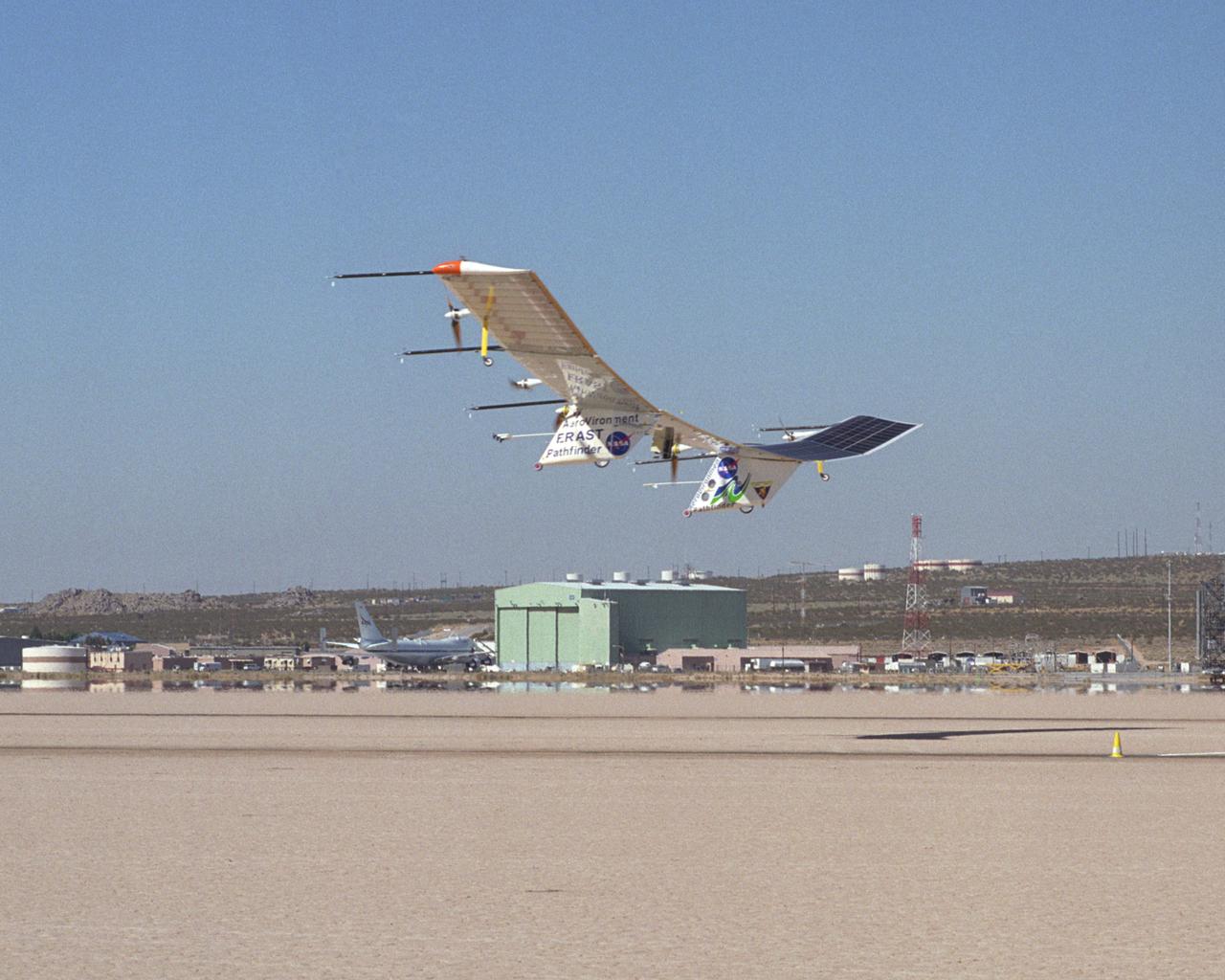 The Pathfinder-Plus solar aircraft flies past NASA Dryden's space shuttle hangar and shuttle carrier aircraft as it descends for landing on Rogers Dry Lake.