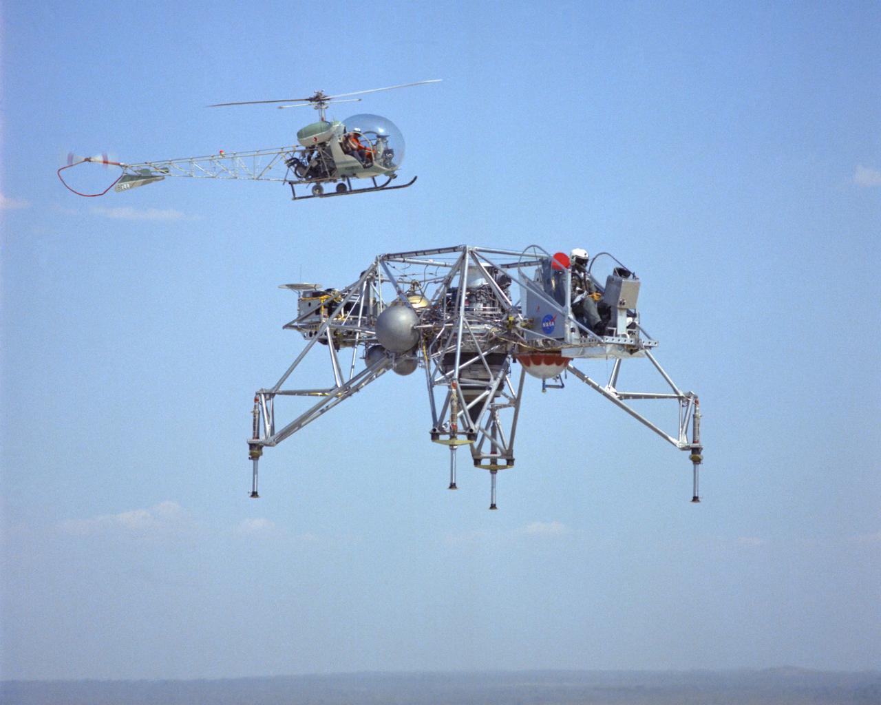 LLRV flight #1-16-61F with Bell 47 Helicopter providing chase support. The use of chase planes was a critical part of flight research well before the establishment of what was then called the NACA Muroc Flight Test Unit in September 1947 (now the NASA Dryden Flight Research Center). They act as a second set of eyes for the research pilot, warning him of any problems. When test flights of the LLRV began in October 1964, chase support for the vehicle was supplied by a Bell 47 helicopter. It could hover close by, providing information such as altitude and descent rate. LLRV test operations were phased out in late 1966 and early 1967. When Apollo planning was underway in 1960, NASA was looking for a simulator to profile the descent to the Moon's surface. Three concepts surfaced: an electronic simulator, a tethered device, and the ambitious Dryden contribution, a free-flying vehicle. All three became serious projects, but eventually the NASA Flight Research Center’s (FRC) Lunar Landing Research Vehicle (LLRV) became the most significant one. After conceptual planning and meetings with engineers from Bell Aerosystems Company, Buffalo, N.Y., NASA FRC issued a $3.6 million production contract awarded in 1963, for delivery of the first of two vehicles for flight studies. Built of tubular aluminum alloy like a giant four-legged bedstead, the vehicle was to simulate a lunar landing profile from around 1500 feet to the Moon’s surface. The LLRV had a turbofan engine mounted vertically in a gimbal, with 4200 pounds of thrust. The engine, lifted the vehicle up to the test altitude and was then throttled back to support five-sixths of the vehicle's weight, thus simulating the reduced gravity of the Moon. Two lift rockets with thrust that could be varied from 100 to 500 pounds handled the LLRV's rate of descent and horizontal translations. Sixteen smaller rockets, mounted in pairs, gave the pilot control in pitch, yaw, and roll. The pilot’s platform extended forward between t