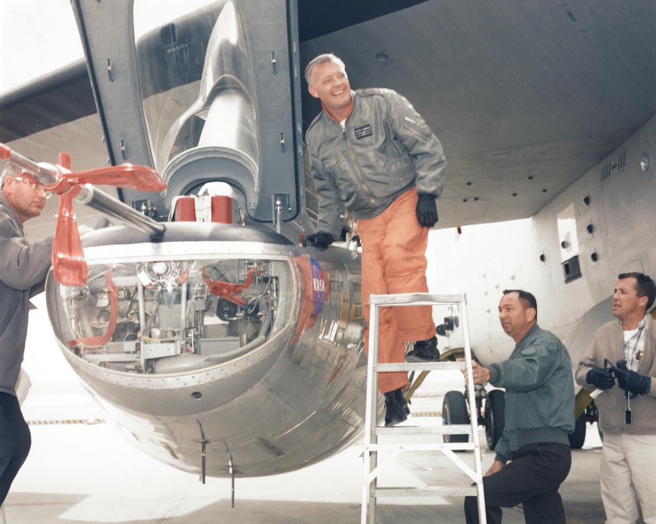 NASA research pilot Milt Thompson is helped into the cockpit of the M2-F2 lifting body research aircraft at NASA’s Flight Research Center (now the Dryden Flight Research Center). The M2-F2 is attached to a wing pylon under the wing of NASA’s B-52 mothership. The flight was a captive flight with the pilot on-board. Milt Thompson flew in the lifting body throughout the flight, but it was never dropped from the mothership.