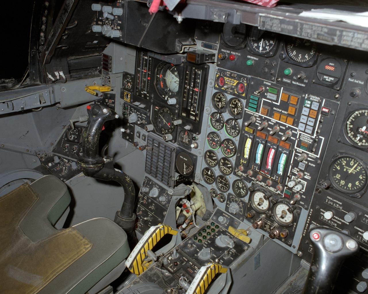 View of the left cockpit and pilot's seat of the F-111 MAW aircraft. Unlike most fighter aircraft of the time, the F-111 had side-by-side seating. The pilot sat on the left side, and the weapons systems officer on the right. Both had control sticks to fly the aircraft. The two yellow and black striped handles would be used in an emergency to eject the entire F-111 cockpit. The F-111 also did not have ejection seats, but used a capsule.