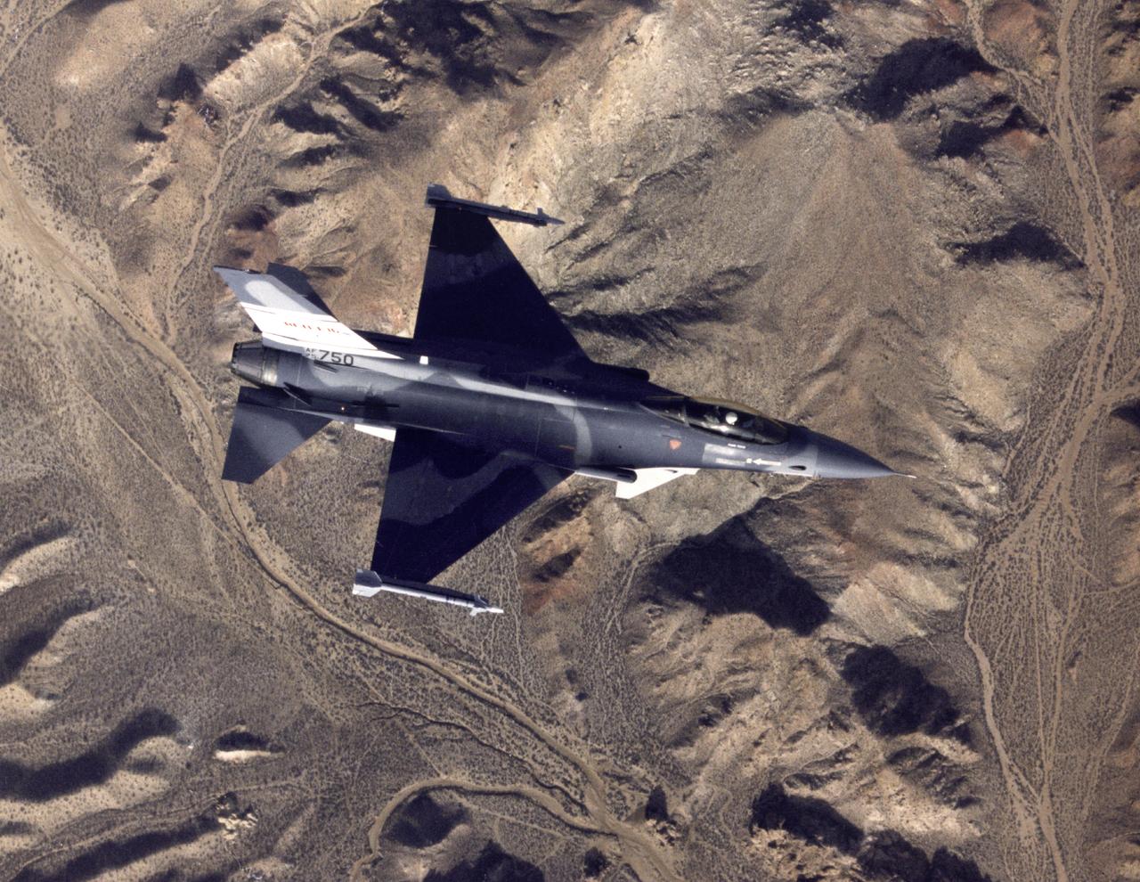 Overhead photograph of the AFTI F-16 painted in a non-standard gray finish, taken during a research flight in 1989. The two sensor pods are visible on the fuselage just forward of the wings and one of the two chin canards can be seen as a light-colored triangle ahead of one of the pods. A Sidewinder air-to-air missile is mounted on each wing tip.