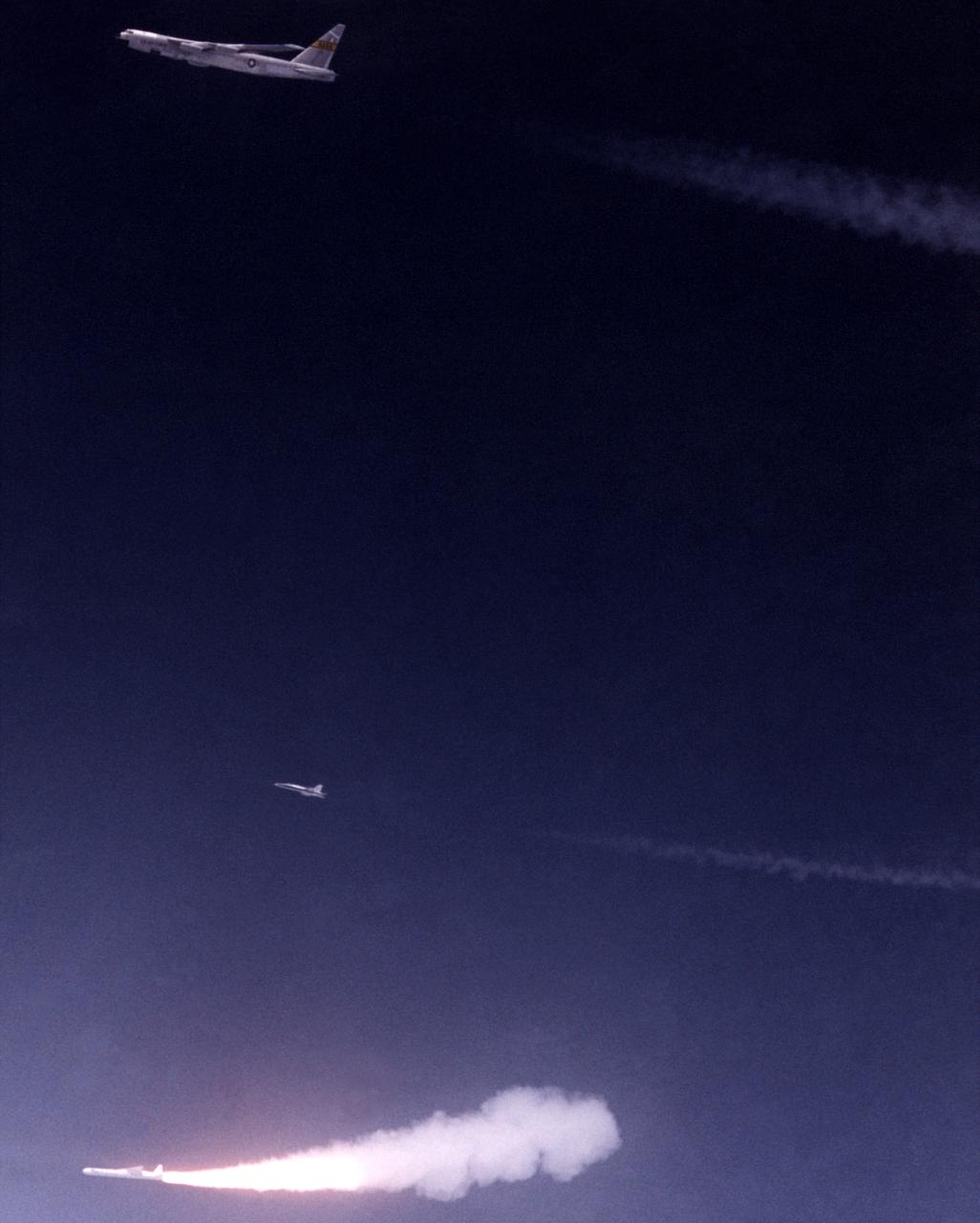 Against the midnight blue of a high-altitude sky, Orbital Sciences’ Pegasus winged rocket booster ignites after being dropped from NASA’s B-52 mothership on a July 1991 flight. A NASA chase plane for the flight is also visible above the rocket and below the B-52.