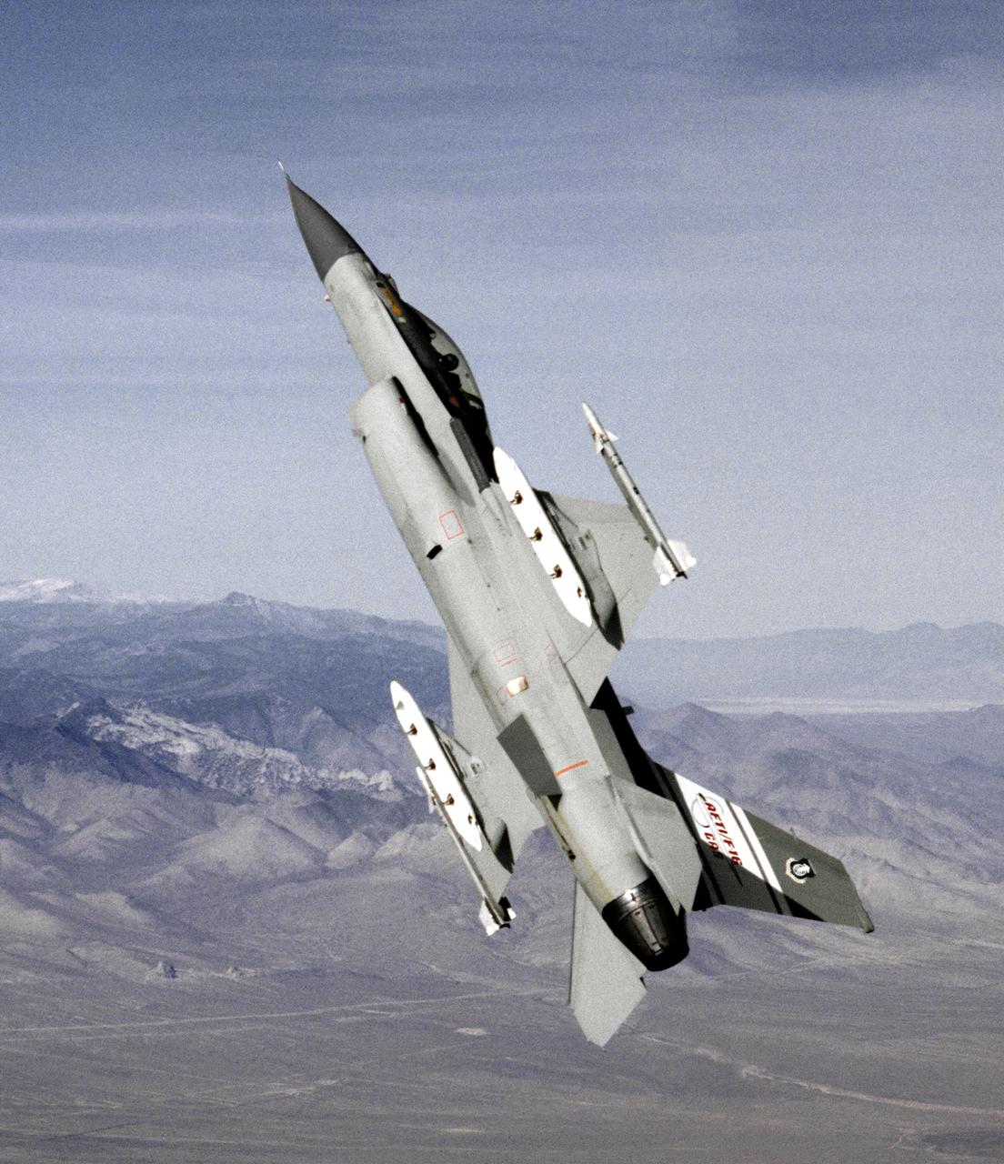 The AFTI F-16 flying at high angle of attack, shown in the final configuration and paint finish. Dummy Sidewinder air-to-air missles are attached to the wing tips. The white objects visible on the wing racks represent practice bomb dispensers, used in weapon tests. 