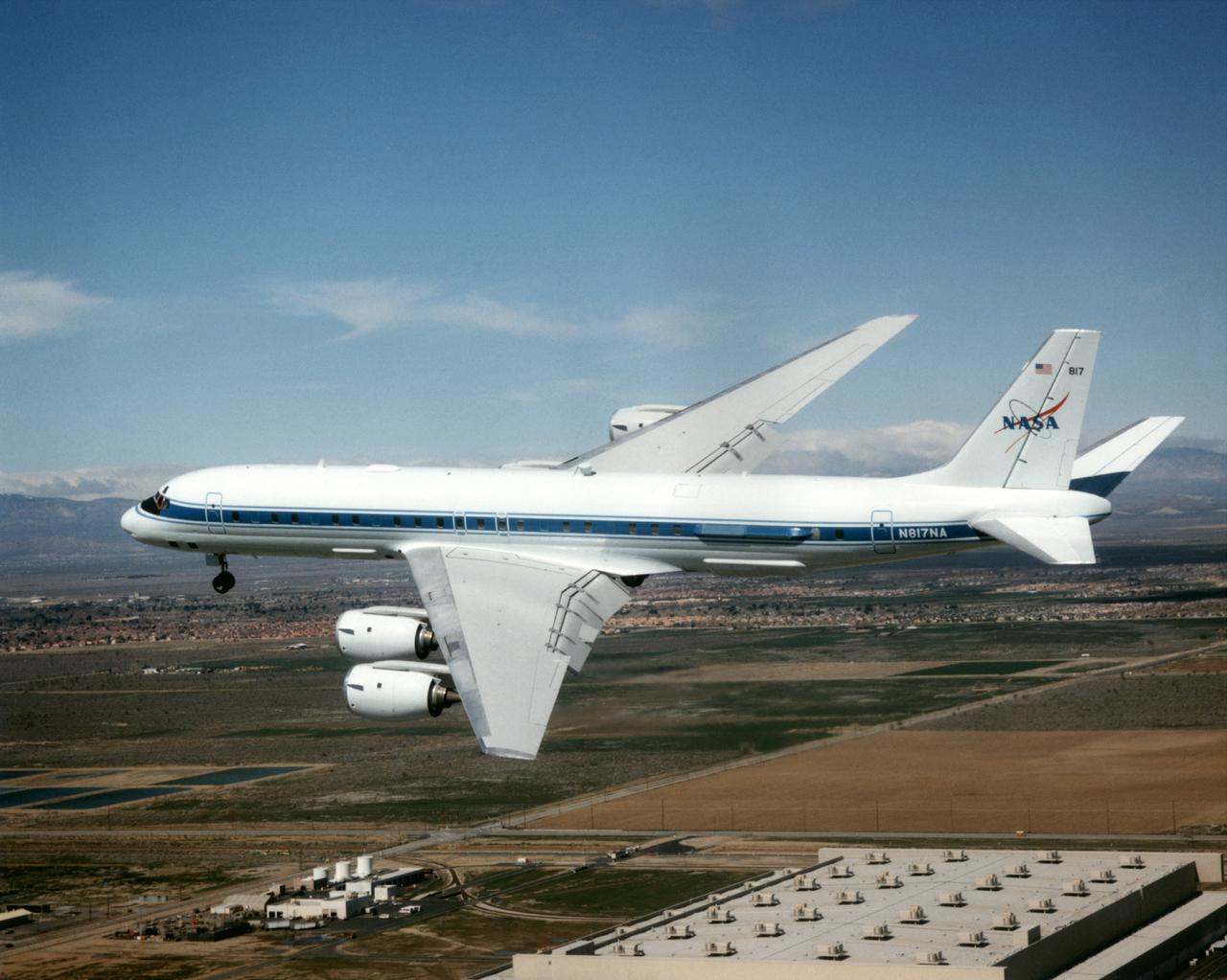The DC-8 Airborne Laboratory in a left banking turn above the airport at Palmdale, California. The right wing is silhouetted against the blue sky, while the left wing contrasts with the desert terrain. The former airliner is a "dash-72" model and has a range of 5,400 miles. The craft can stay airborne for 12 hours and has an operational speed range between 300 and 500 knots. The research flights are made at between 500 and 41,000 feet. The aircraft can carry up to 30,000 lbs of research/science payload equipment installed in 15 mission-definable spaces.