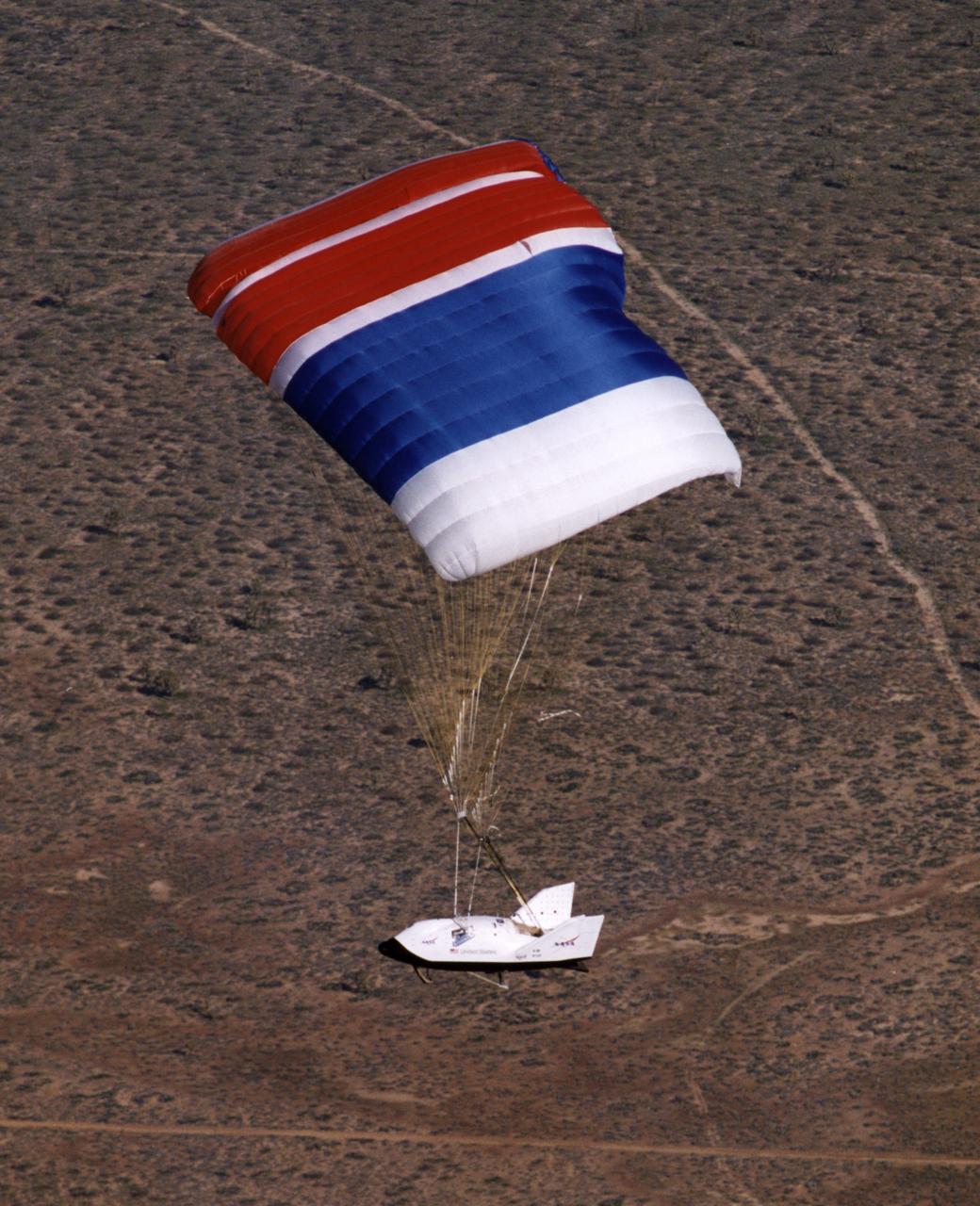The X-38 Crew Return Vehicle descends under its steerable parafoil over the California desert during its first free flight in March 1998 at the Dryden Flight Research Center, Edwards, California.