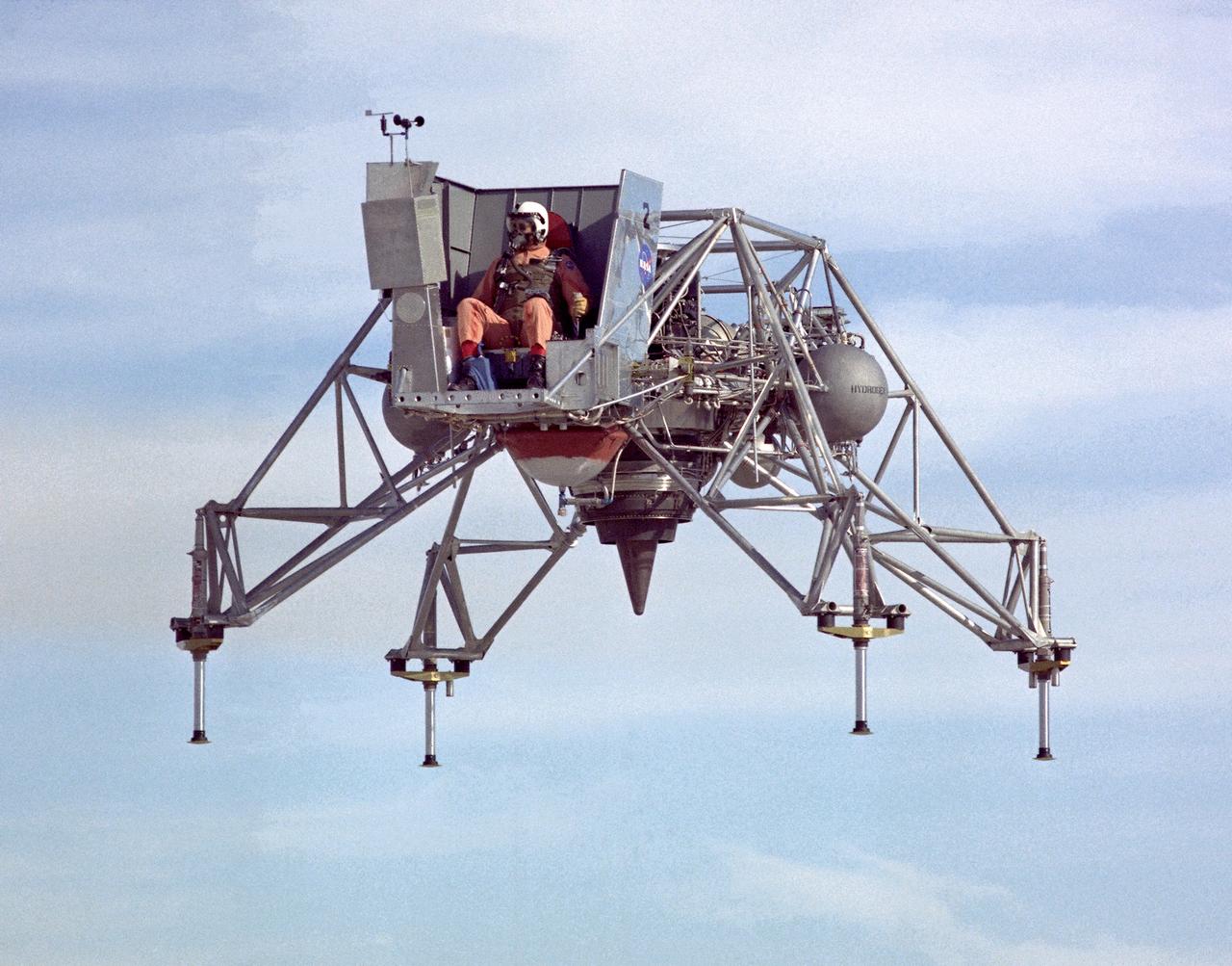 In this 1967 NASA Flight Reserch Center photograph the Lunar Landing Research Vehicle (LLRV) is viewed from the front. This photograph provideds a good view of the pilot’s platform with the restrictive cockpit view like that of he real Lunar Module (LM) When Apollo planning was underway in 1960, NASA was looking for a simulator to profile the descent to the Moon's surface. Three concepts surfaced: an electronic simulator, a tethered device, and the ambitious Dryden contribution, a free-flying vehicle. All three became serious projects, but eventually the NASA Flight Research Center’s (FRC) Lunar Landing Research Vehicle (LLRV) became the most significant one. After conceptual planning and meetings with engineers from Bell Aerosystems Company, Buffalo, N.Y., NASA FRC issued a $3.6 million production contract awarded in 1963, for delivery of the first of two vehicles for flight studies.  Built of tubular aluminum alloy like a giant four-legged bedstead, the vehicle was to simulate a lunar landing profile from around 1500 feet to the Moon’s surface. The LLRV had a turbofan engine mounted vertically in a gimbal, with 4200 pounds of thrust. The engine, lifted the vehicle up to the test altitude and was then throttled back to support five-sixths of the vehicle's weight, thus simulating the reduced gravity of the Moon. Two lift rockets with thrust that could be varied from 100 to 500 pounds handled the LLRV's rate of descent and horizontal translations. Sixteen smaller rockets, mounted in pairs, gave the pilot control in pitch, yaw, and roll.. The pilot’s platform extended forward between two legs while an electronics platform, similarly located, extended rearward. The pilot had a zero-zero ejection seat that would then lift him away to safety.  The two LLRVs were shipped from Bell to the FRC in April 1964, with program emphasis on vehicle No. 1. The first flight, Oct. 30, 1964, NASA research pilot Joe Walker flew it three times for a total of just under 60 seconds