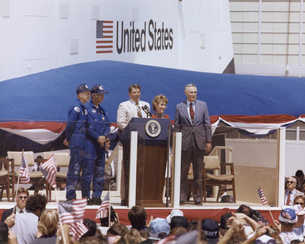 President Ronald Reagan speaks to a crowd of more than 45,000 people at NASA's Dryden Flight Research Center following the landing of STS-4 on July 4, 1982. To the right of the President are Mrs. Reagan and NASA Administrator James M. Beggs. To the left are STS-4 Columbia astronauts Thomas K. Mattingly and Henry W. Hartsfield, Jr. Prototype Space Shuttle Enterprise is in the background.