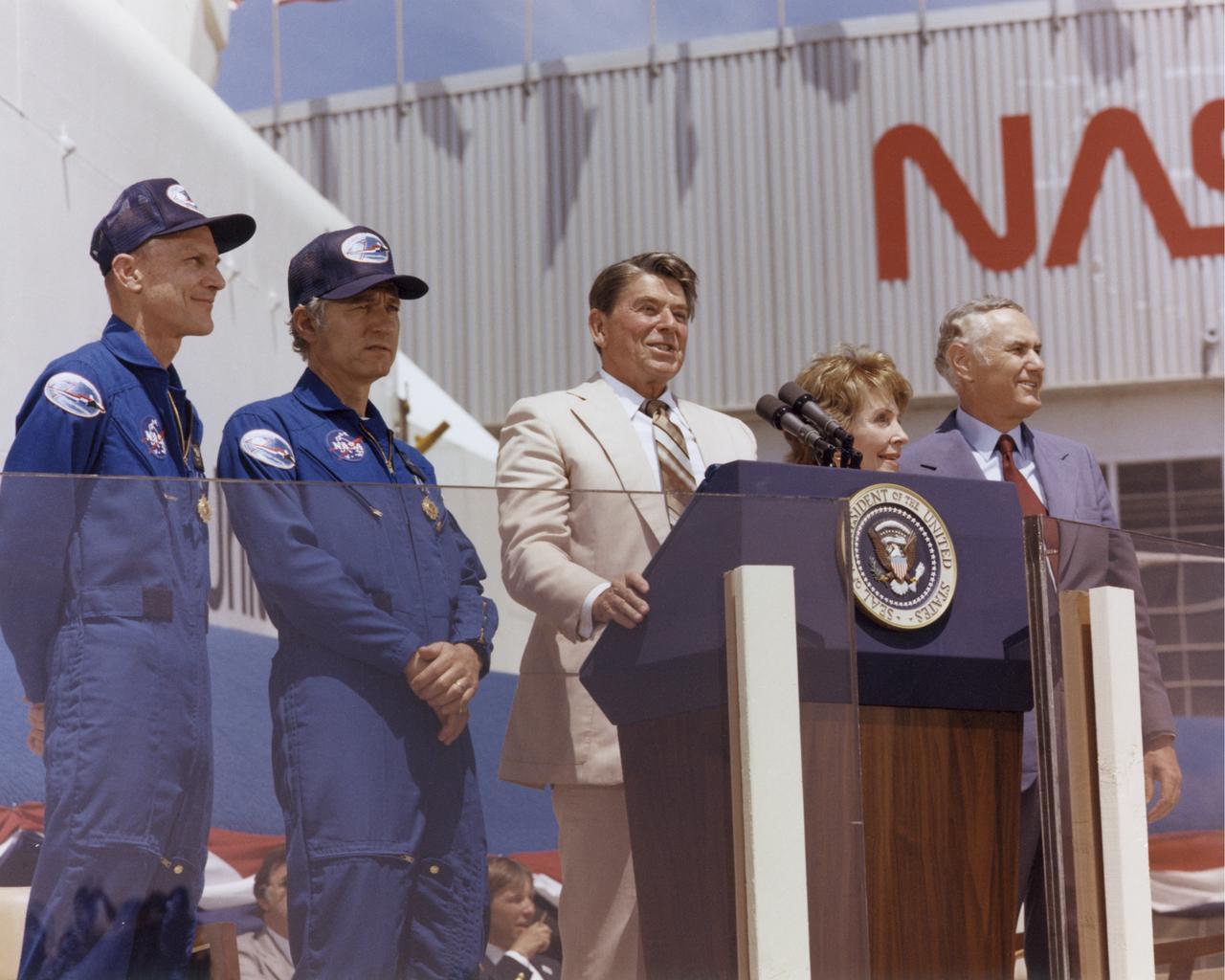 President Ronald Reagan speaks to a crowd of more than 45,000 people at NASA's Dryden Flight Research Center following the landing of STS-4 on July 4, 1982. To the right of the President are Mrs. Reagan and NASA Administrator James M. Beggs. To the left are STS-4 Columbia astronauts Thomas K. Mattingly and Henry W. Hartsfield, Jr. Prototype Space Shuttle Enterprise is in the background.