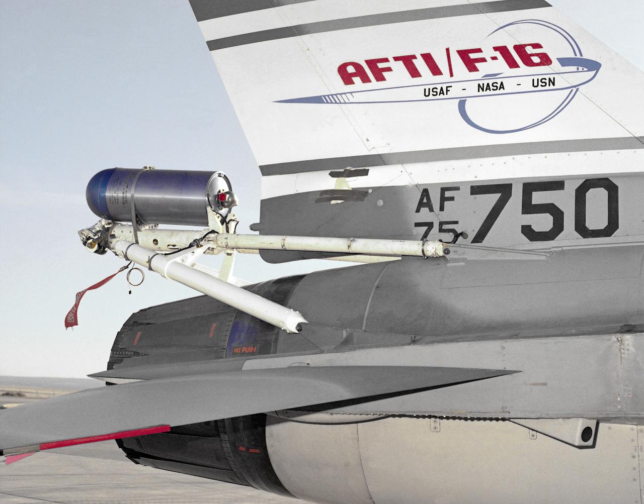 A close-up photo of the spin chute mounted on the rear fuselage of the AFTI F-16, a safety device designed to prevent the loss of aircraft in spin conditions. Under some circumstances, pilots cannot recover from spins using normal controls. It these instances, the spin chute is deployed, thus "breaking" the spin and enabling the pilot to recover. The spin chute is held in a metal cylinder attached to the AFTI F-16 by four tubes, a structure strong enough to withstand the shock of the spin chute opening. Unlike the air probe in the last photo, spin chutes are not standard equipment on research or prototype aircraft but are commonly attached expressly for actual spin tests.
