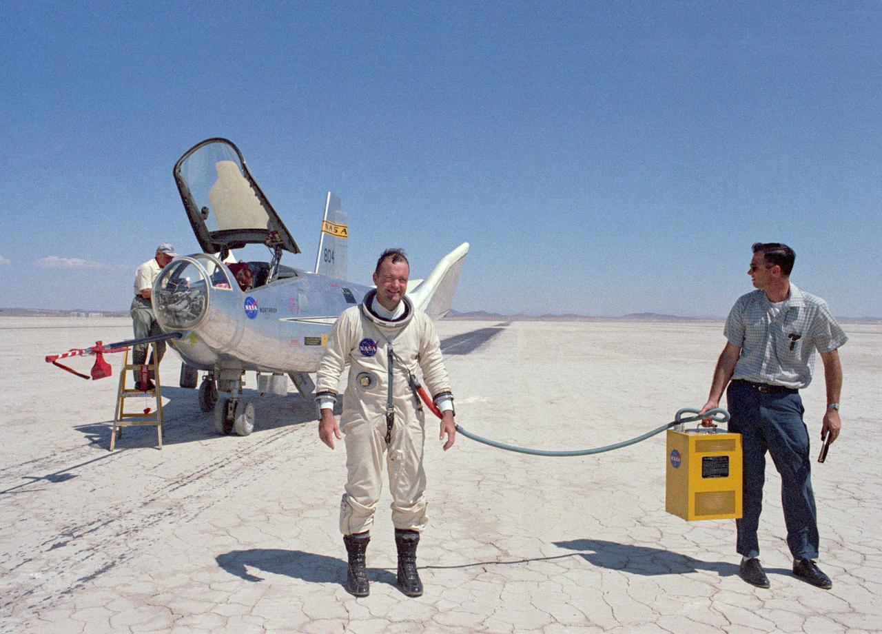 NASA research pilot Bill Dana after his fourth free flight (1 glide and 3 powered) in the HL-10. This particular flight reached a maximum speed of Mach 1.45. Dana made a total of nine HL-10 flights (1 glide and 8 powered), and his lifting body experience as a whole included several car tow and 1 air tow flights in the M2-F1; 4 glide and 15 powered flights in the M2-F3; and 2 powered flights in the X-24B. He is wearing a pressure suit for protection against the cockpit depressurizing at high altitudes. The air conditioner box held by the ground crewman provides cool air to prevent overheating.