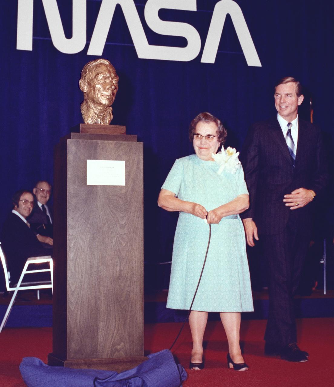 On March 26, 1976, the NASA Flight Research Center opened its doors to hundreds of guests for the dedication of the center in honor of Hugh Latimer Dryden. The dedication was very much a local event; following Center Director David Scott’s opening remarks, the Antelope Valley High School’s symphonic band played the national anthem. Invocation was given followed by recognition of the invited guests. Dr. Hugh Dryden, a man of total humility, received praise from all those present. Dryden, who died in 1965, had been a pioneering aeronautical scientist who became director of the National Advisory Committee for Aeronautics (NACA) in 1949 and then deputy administrator of the NACA’s successor, NASA, in 1958. Very much interested in flight research, he had been responsible for establishing a permanent facility at the location later named in his honor.  As Center Director David Scott looks on, Mrs. Hugh L. Dryden (Mary Libbie Travers) unveils the memorial to her husband at the dedication ceremony.On March 26, 1976, the NASA Flight Research Center opened its doors to hundreds of guests for the dedication of the center in honor of Hugh Latimer Dryden.
