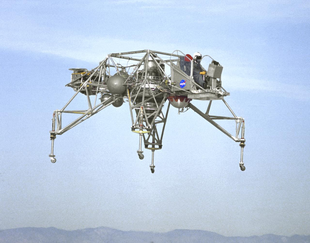 In this NASA Flight Reserch Center photograph the Lunar Landing Research Vehicle (LLRV) number 1 is shown in flight. When Apollo planning was underway in 1960, NASA was looking for a simulator to profile the descent to the Moon's surface. Three concepts surfaced: an electronic simulator, a tethered device, and the ambitious Dryden contribution, a free-flying vehicle. All three became serious projects, but eventually the NASA Flight Research Center's (FRC) Landing Research Vehicle (LLRV) became the most significant one. Hubert M. Drake is credited with originating the idea, while Donald Bellman and Gene Matranga were senior engineers on the project, with Bellman, the project manager. Simultaneously, and independently, Bell Aerosystems Company, Buffalo, N.Y., a company with experience in vertical takeoff and landing (VTOL) aircraft, had conceived a similar free-flying simulator and proposed their concept to NASA headquarters. NASA Headquarters put FRC and Bell together to collaborate. The challenge was; to allow a pilot to make a vertical landing on Earth in a simulated Moon environment, one sixth of the Earth's gravity and with totally transparent aerodynamic forces in a "free flight" vehicle with no tether forces acting on it.  Built of tubular aluminum like a giant four-legged bedstead, the vehicle was to simulate a lunar landing profile from around 1500 feet to the Moon's surface. To do this, the LLRV had a General Electric CF-700-2V turbofan engine mounted vertically in gimbals, with 4200 pounds of thrust. The engine, using JP-4 fuel, got the vehicle up to the test altitude and was then throttled back to support five-sixths of the vehicle's weight, simulating the reduced gravity of the Moon. Two hydrogen-peroxide lift rockets with thrust that could be varied from 100 to 500 pounds handled the LLRV's rate of descent and horizontal translations. Sixteen smaller hydrogen-peroxide rockets, mounted in pairs, gave the pilot control in pitch, yaw, and roll. On the LLRV,