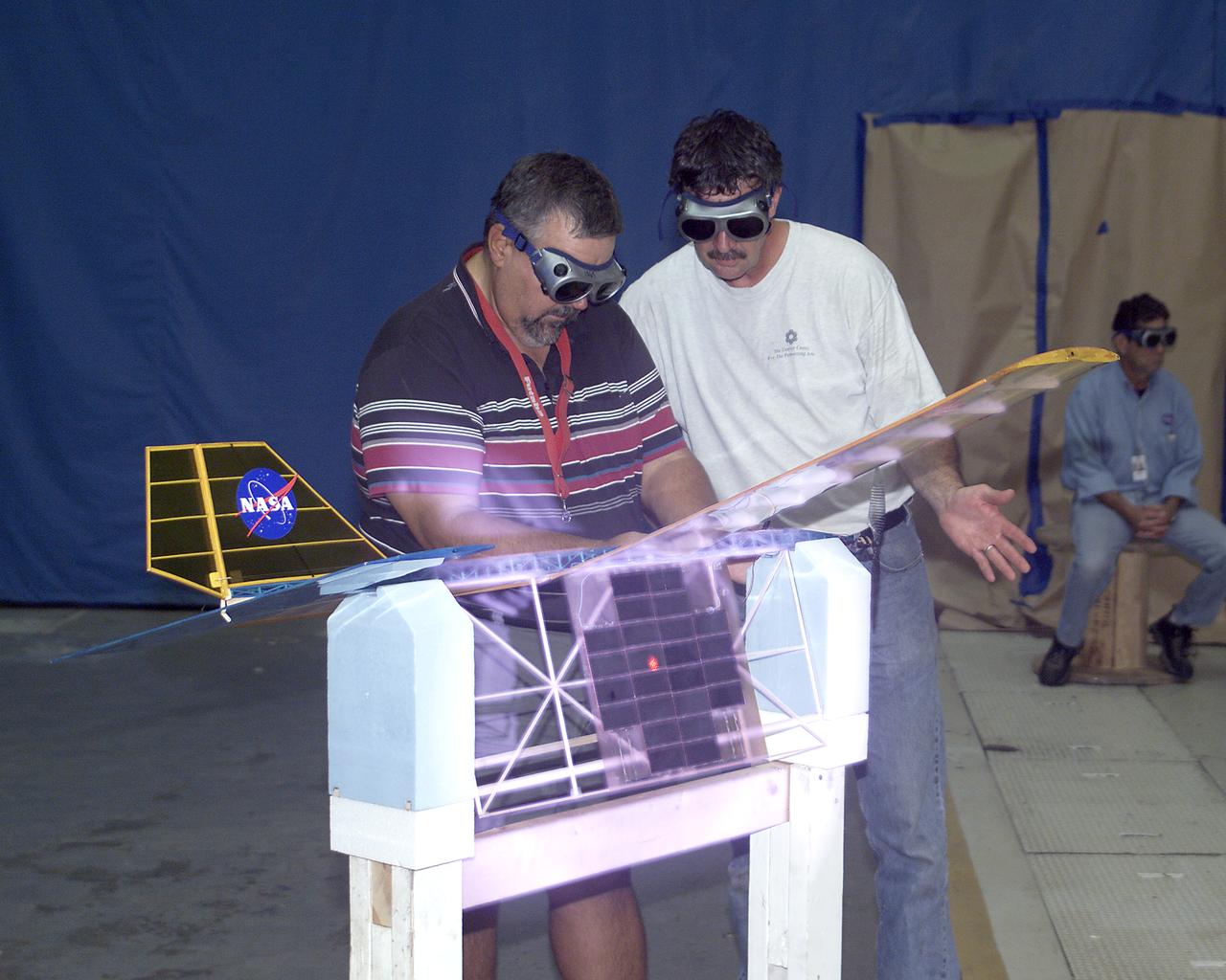 With a laser beam centered on its solar panel, a lightweight model aircraft is checked out by technician Tony Frakowiak and researcher Tim Blackwell before its power-beamed demonstration flight.