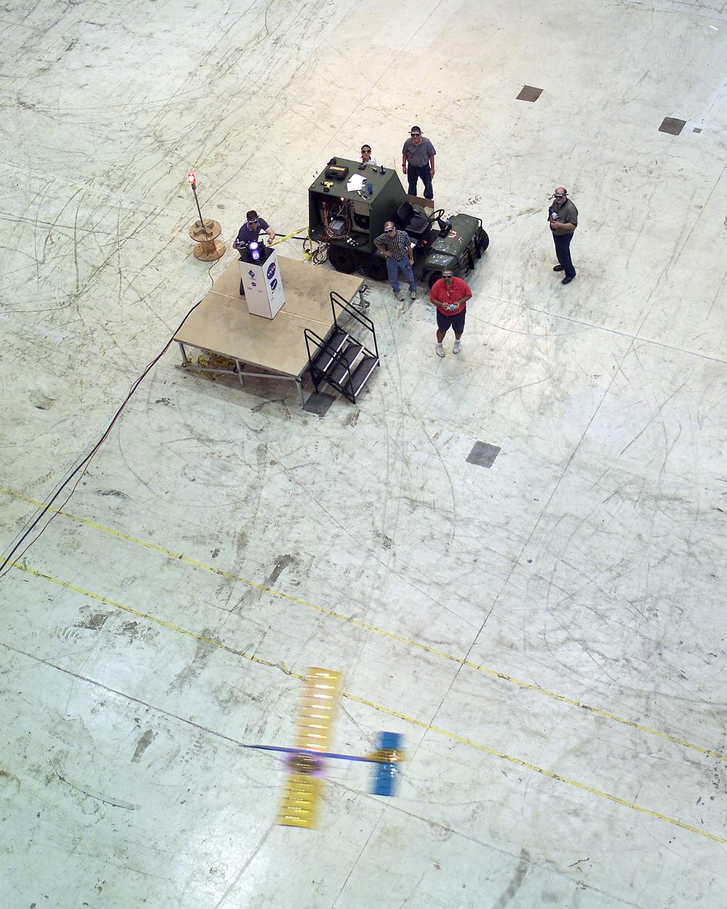 Powered by a laser beam directed at it from a center pedestal, a lightweight model plane makes the first flight of an aircraft powered by laser energy inside a building at NASA's Marshall Space Flight Center.