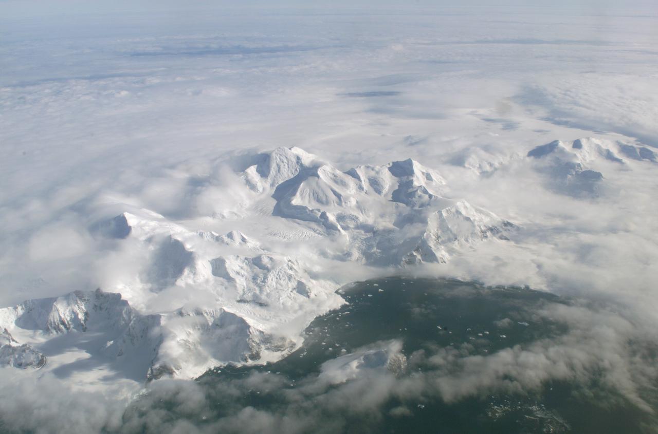 An AirSAR 2004 view from the DC-8 as it approaches the Larsen Ice Shelf, which is part of the Antarctic Peninsula. AirSAR 2004 is a three-week expedition in Central and South America by an international team of scientists that is using an all-weather imaging tool, called the Airborne Synthetic Aperture Radar (AirSAR), located onboard NASA's DC-8 airborne laboratory. Scientists from many parts of the world are combining ground research with NASA's AirSAR technology to improve and expand on the quality of research they are able to conduct. These photos are from the DC-8 aircraft while flying an AirSAR mission over Antarctica. The Antarctic Peninsula is more similar to Alaska and Patagonia than to the rest of the Antarctic continent. It is drained by fast glaciers, receives abundant precipitation, and melts significantly in the summer months. In recent decades, the Peninsula has experienced significant atmospheric warming (about 2 degrees C since 1950), which has triggered a vast and spectacular retreat of its floating ice shelves, glacier reduction, a decrease in permanent snow cover and a lengthening of the melt season. As a result, the contribution to sea level from this region could be rapid and substantial. With an area of 120,000 km, or ten times the Patagonia ice fields, the Peninsula could contribute as much as 0.4mm/yr sea level rise, which would be the largest single contribution to sea level from anywhere in the world.  This region is being studied by NASA using a DC-8 equipped with the Airborne Synthetic Aperture Radar developed by scientists from NASA’s Jet Propulsion Laboratory. AirSAR will provide a baseline model and unprecedented mapping of the region. This data will make it possible to determine whether the warming trend is slowing, continuing or accelerating. AirSAR will also provide reliable information on ice shelf thickness to measure the contribution of the glaciers to sea level.