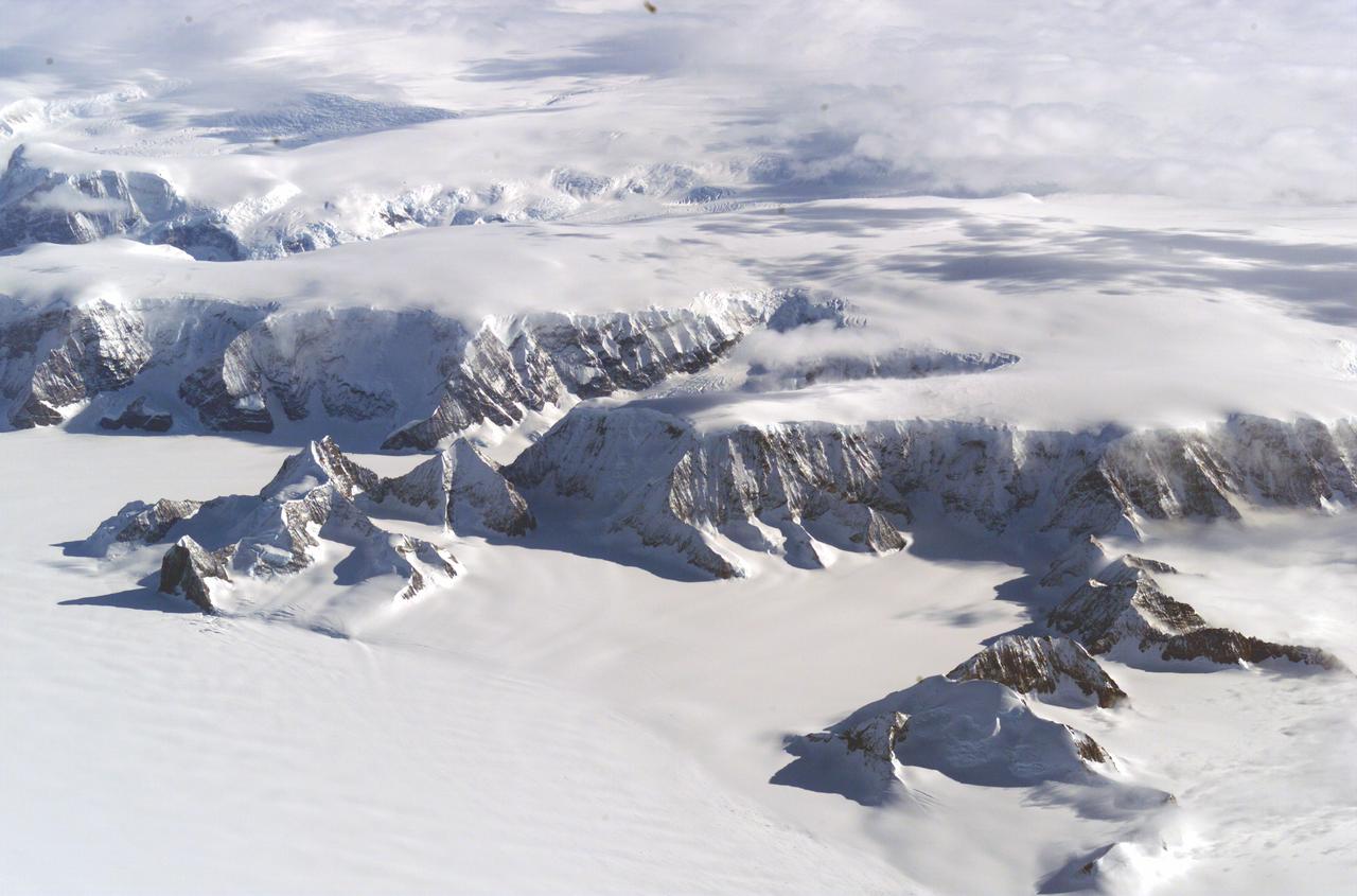 The Larsen Ice Shelf in Antarctica viewed from NASA's DC-8 aircraft during the AirSAR 2004 campaign. AirSAR 2004 is a three-week expedition in Central and South America by an international team of scientists that is using an all-weather imaging tool, called the Airborne Synthetic Aperture Radar (AirSAR), located onboard NASA's DC-8 airborne laboratory. Scientists from many parts of the world are combining ground research with NASA's AirSAR technology to improve and expand on the quality of research they are able to conduct. These photos are from the DC-8 aircraft while flying an AirSAR mission over Antarctica. The Antarctic Peninsula is more similar to Alaska and Patagonia than to the rest of the Antarctic continent. It is drained by fast glaciers, receives abundant precipitation, and melts significantly in the summer months. In recent decades, the Peninsula has experienced significant atmospheric warming (about 2 degrees C since 1950), which has triggered a vast and spectacular retreat of its floating ice shelves, glacier reduction, a decrease in permanent snow cover and a lengthening of the melt season. As a result, the contribution to sea level from this region could be rapid and substantial. With an area of 120,000 km, or ten times the Patagonia ice fields, the Peninsula could contribute as much as 0.4mm/yr sea level rise, which would be the largest single contribution to sea level from anywhere in the world.  This region is being studied by NASA using a DC-8 equipped with the Airborne Synthetic Aperture Radar developed by scientists from NASA’s Jet Propulsion Laboratory. AirSAR will provide a baseline model and unprecedented mapping of the region. This data will make it possible to determine whether the warming trend is slowing, continuing or accelerating. AirSAR will also provide reliable information on ice shelf thickness to measure the contribution of the glaciers to sea level.
