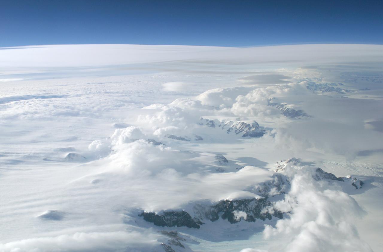 The Larsen Ice Shelf in Antarctica viewed from NASA's DC-8 aircraft during the AirSAR 2004 campaign. AirSAR 2004 is a three-week expedition in Central and South America by an international team of scientists that is using an all-weather imaging tool, called the Airborne Synthetic Aperture Radar (AirSAR), located onboard NASA's DC-8 airborne laboratory. Scientists from many parts of the world are combining ground research with NASA's AirSAR technology to improve and expand on the quality of research they are able to conduct. These photos are from the DC-8 aircraft while flying an AirSAR mission over Antarctica. The Antarctic Peninsula is more similar to Alaska and Patagonia than to the rest of the Antarctic continent. It is drained by fast glaciers, receives abundant precipitation, and melts significantly in the summer months. In recent decades, the Peninsula has experienced significant atmospheric warming (about 2 degrees C since 1950), which has triggered a vast and spectacular retreat of its floating ice shelves, glacier reduction, a decrease in permanent snow cover and a lengthening of the melt season. As a result, the contribution to sea level from this region could be rapid and substantial. With an area of 120,000 km, or ten times the Patagonia ice fields, the Peninsula could contribute as much as 0.4mm/yr sea level rise, which would be the largest single contribution to sea level from anywhere in the world.  This region is being studied by NASA using a DC-8 equipped with the Airborne Synthetic Aperture Radar developed by scientists from NASA’s Jet Propulsion Laboratory. AirSAR will provide a baseline model and unprecedented mapping of the region. This data will make it possible to determine whether the warming trend is slowing, continuing or accelerating. AirSAR will also provide reliable information on ice shelf thickness to measure the contribution of the glaciers to sea level.