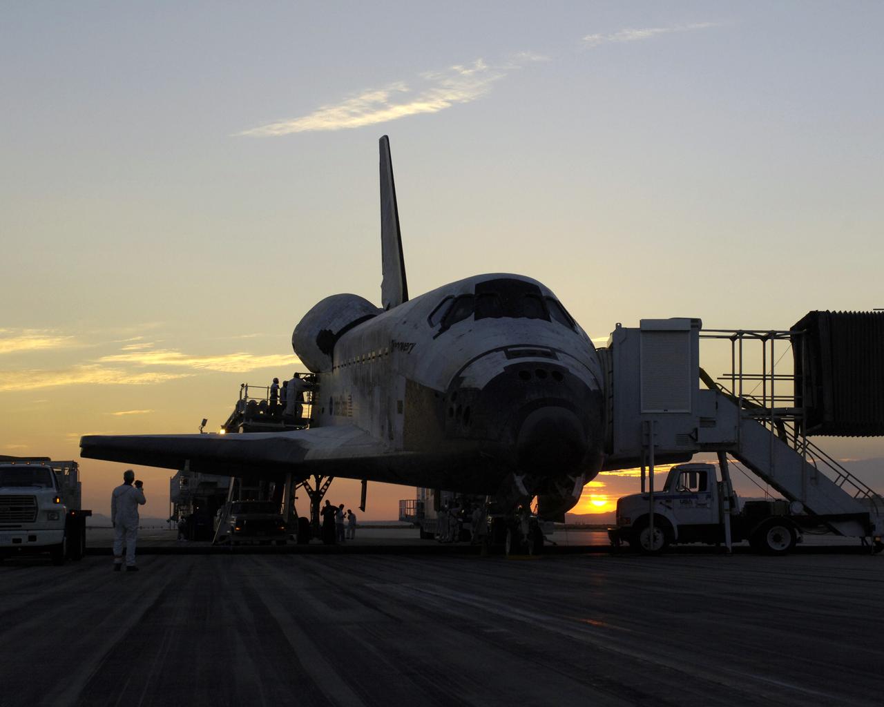 The sun rises on the Space Shuttle Discovery as it rests on the runway at Edwards Air Force Base, California, after a safe landing August 9, 2005 to complete the STS-114 mission. Space Shuttle Discovery landed safely at NASA's Dryden Flight Research Center at Edwards Air Force Base in California at 5:11:22 a.m. PDT this morning, following the very successful 14-day STS-114 return to flight mission.  During their two weeks in space, Commander Eileen Collins and her six crewmates tested out new safety procedures and delivered supplies and equipment the International Space Station.  Discovery spent two weeks in space, where the crew demonstrated new methods to inspect and repair the Shuttle in orbit. The crew also delivered supplies, outfitted and performed maintenance on the International Space Station. A number of these tasks were conducted during three spacewalks.  In an unprecedented event, spacewalkers were called upon to remove protruding gap fillers from the heat shield on Discovery's underbelly. In other spacewalk activities, astronauts installed an external platform onto the Station's Quest Airlock and replaced one of the orbital outpost's Control Moment Gyroscopes.  Inside the Station, the STS-114 crew conducted joint operations with the Expedition 11 crew. They unloaded fresh supplies from the Shuttle and the Raffaello Multi-Purpose Logistics Module. Before Discovery undocked, the crews filled Raffeallo with unneeded items and returned to Shuttle payload bay.  Discovery launched on July 26 and spent almost 14 days on orbit.