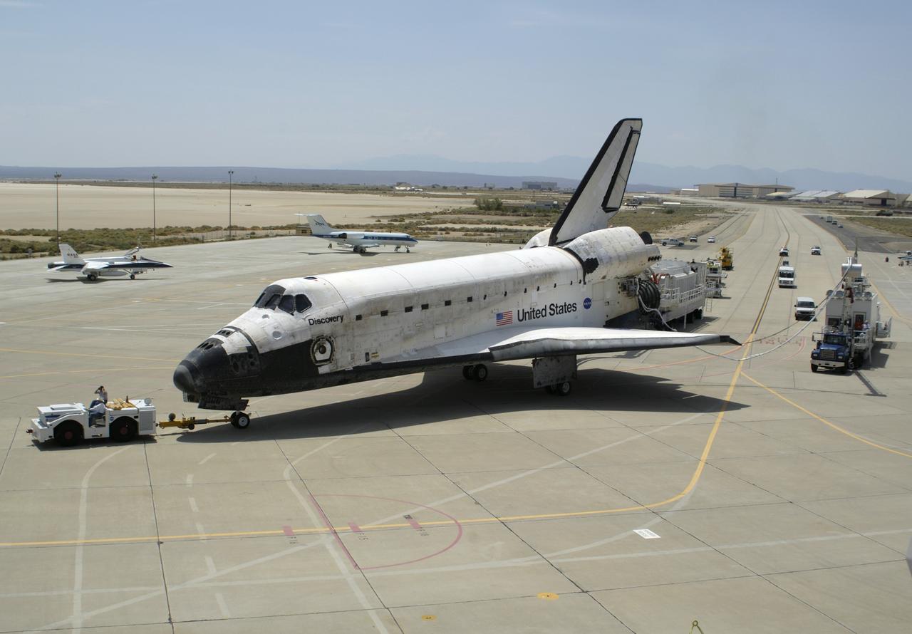 The Space Shuttle Discovery, accompanied by a convoy of recovery vehicles, is towed up the taxiway at NASA's Dryden Flight Research Center at Edwards Air Force Base, California, following its landing on August 9, 2005. Space Shuttle Discovery landed safely at NASA's Dryden Flight Research Center at Edwards Air Force Base in California at 5:11:22 a.m. PDT this morning, following the very successful 14-day STS-114 return to flight mission.  During their two weeks in space, Commander Eileen Collins and her six crewmates tested out new safety procedures and delivered supplies and equipment the International Space Station.  Discovery spent two weeks in space, where the crew demonstrated new methods to inspect and repair the Shuttle in orbit. The crew also delivered supplies, outfitted and performed maintenance on the International Space Station. A number of these tasks were conducted during three spacewalks.  In an unprecedented event, spacewalkers were called upon to remove protruding gap fillers from the heat shield on Discovery's underbelly. In other spacewalk activities, astronauts installed an external platform onto the Station's Quest Airlock and replaced one of the orbital outpost's Control Moment Gyroscopes.  Inside the Station, the STS-114 crew conducted joint operations with the Expedition 11 crew. They unloaded fresh supplies from the Shuttle and the Raffaello Multi-Purpose Logistics Module. Before Discovery undocked, the crews filled Raffeallo with unneeded items and returned to Shuttle payload bay.  Discovery launched on July 26 and spent almost 14 days on orbit.