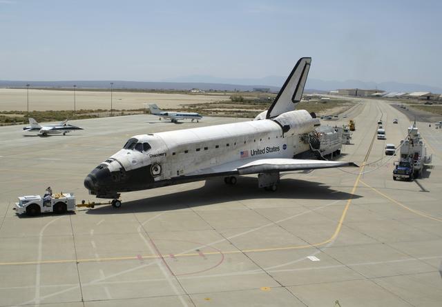 NASA image: Shuttle Discovery, accompanied by recovery vehicles, is towed up the taxiway at NASA's Dryden Flight Research Center following its landing on August 9, 2005