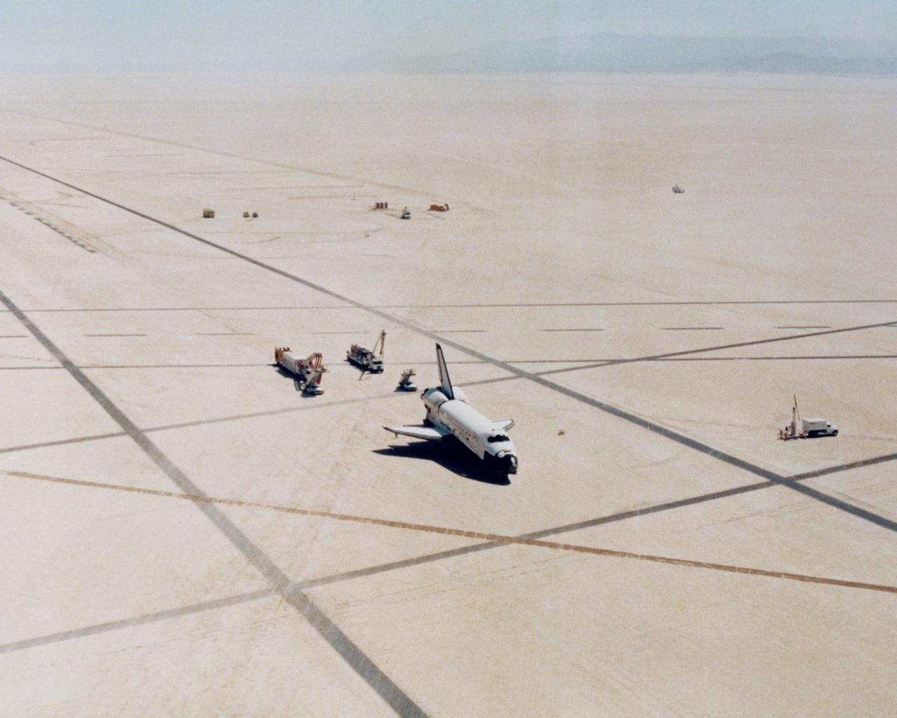 The Space Shuttle Columbia on Rogers Dry lakebed at Edwards AFB after landing to complete its first orbital mission on April 14, 1981. Technicians towed the Shuttle back to the NASA Dryden Flight Research Center for post-flight processing and preparation for a return ferry flight atop a modified 747 to Kennedy Space Center in Florida. (JSC photo # S81-30749)