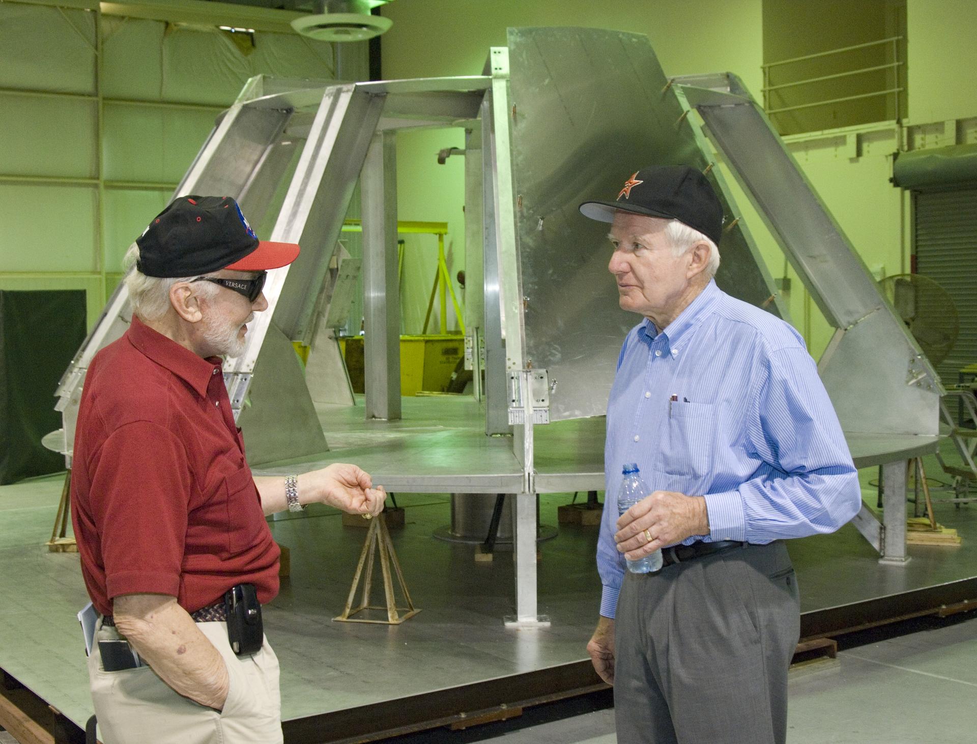 Buzz Aldrin and Vance Brand talking together in front of an Orion fit-check crew module mockup.