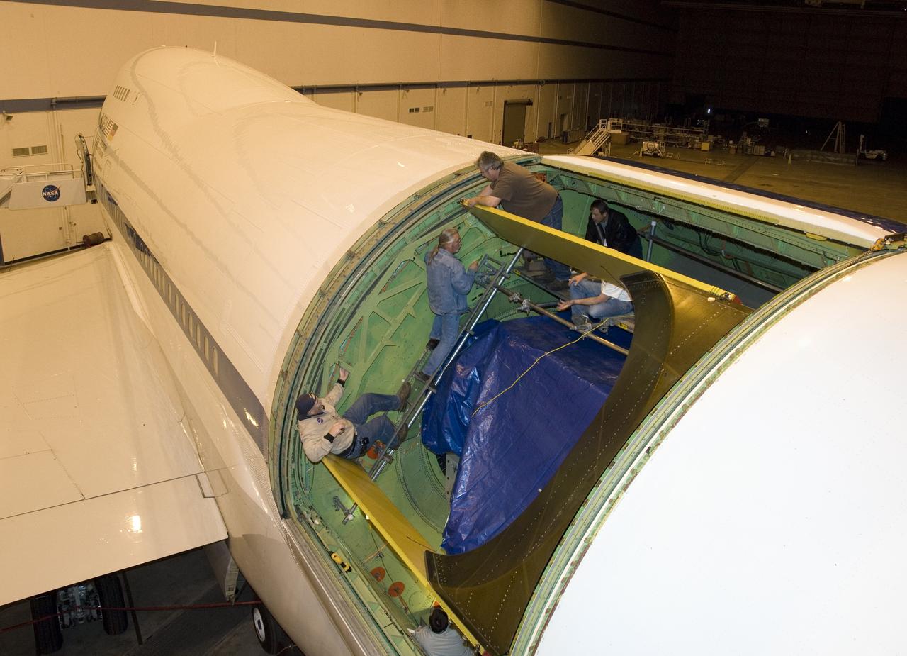 Technicians carefully disassemble portions of the aperture mounting assembly from NASA's SOFIA aircraft in preparation for removal of the telescope.